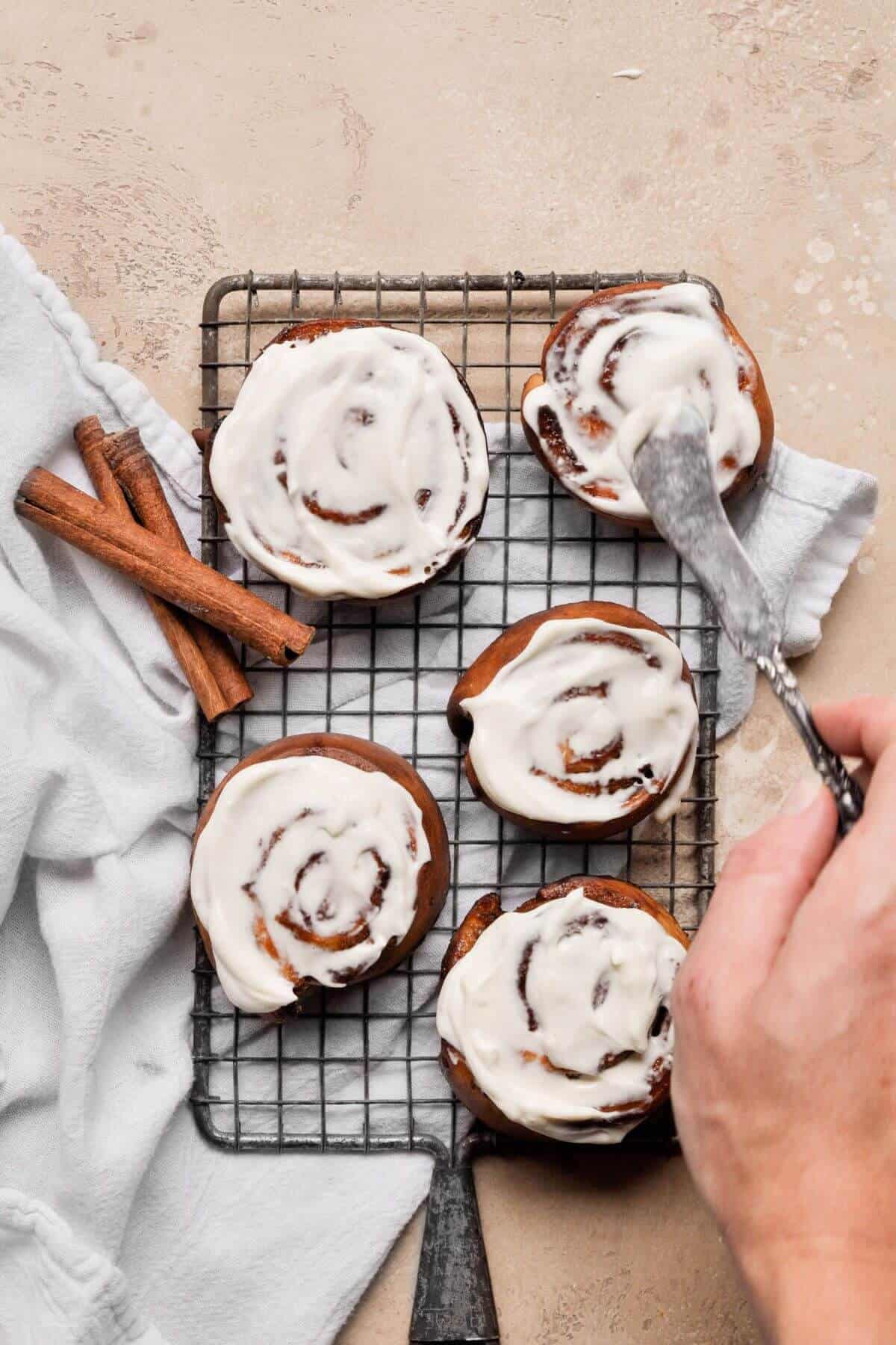 Frosting air fryer cinnamon rolls with cream cheese yogurt frosting.