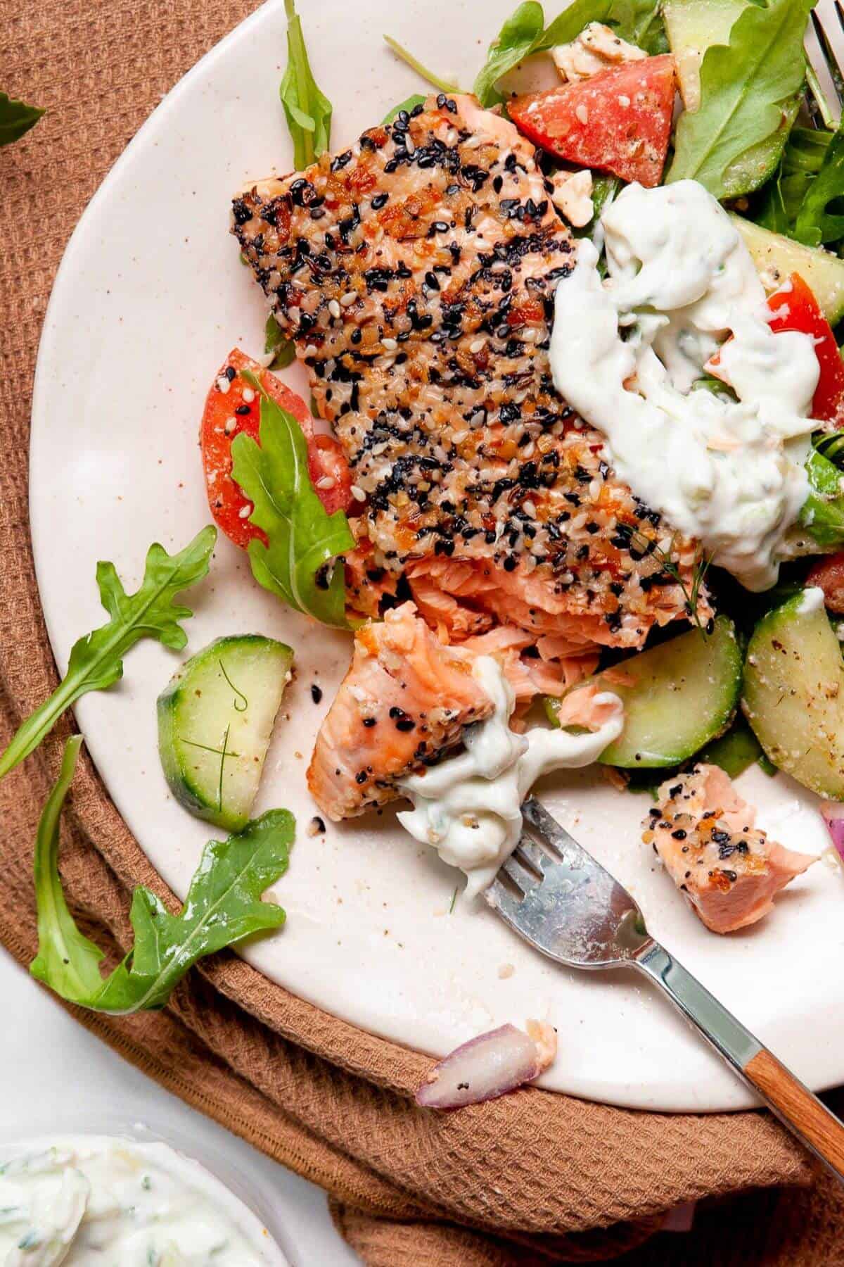 Flaked everything bagel salmon on a fork with cucumber and tomato salad.