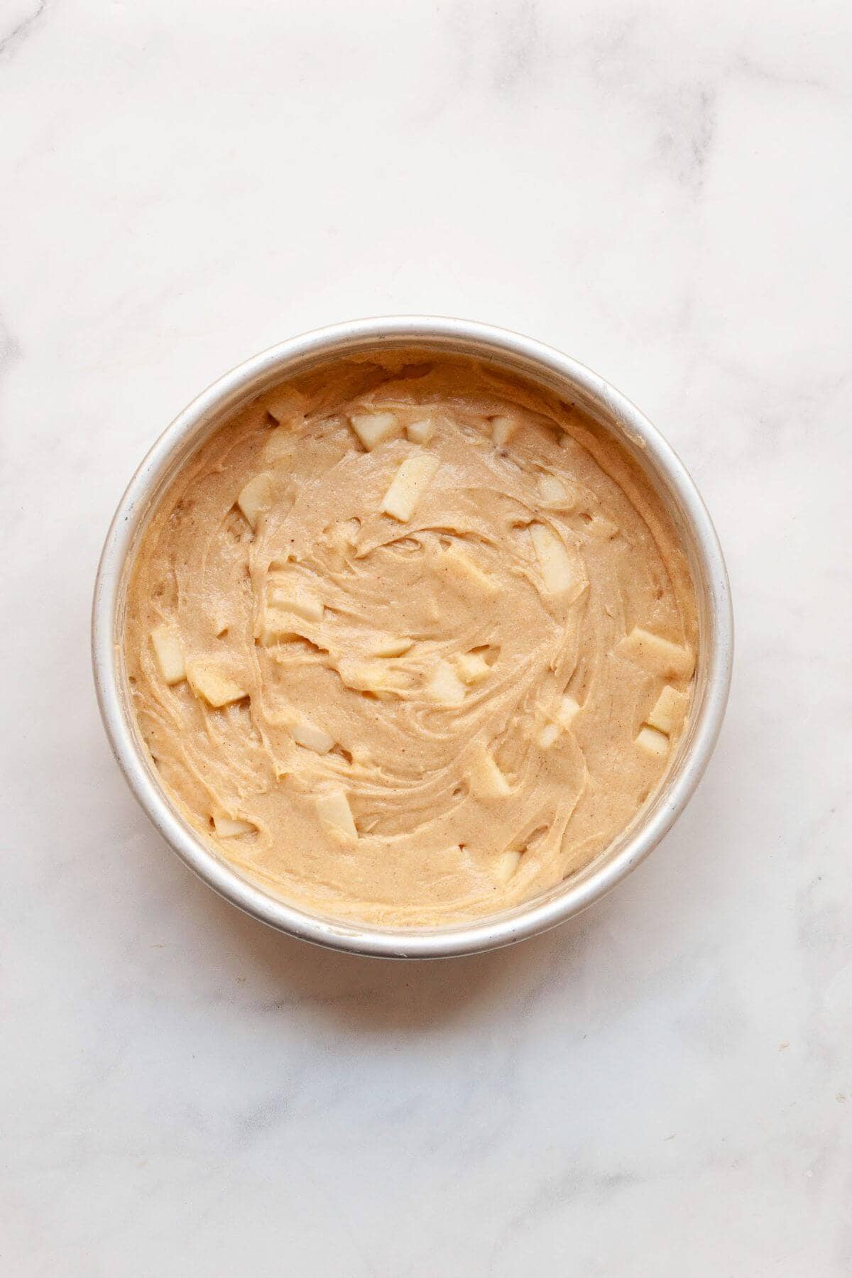 Unbaked gluten-free apple cake batter with fresh apple chunks in a cake pan, ready to bake.