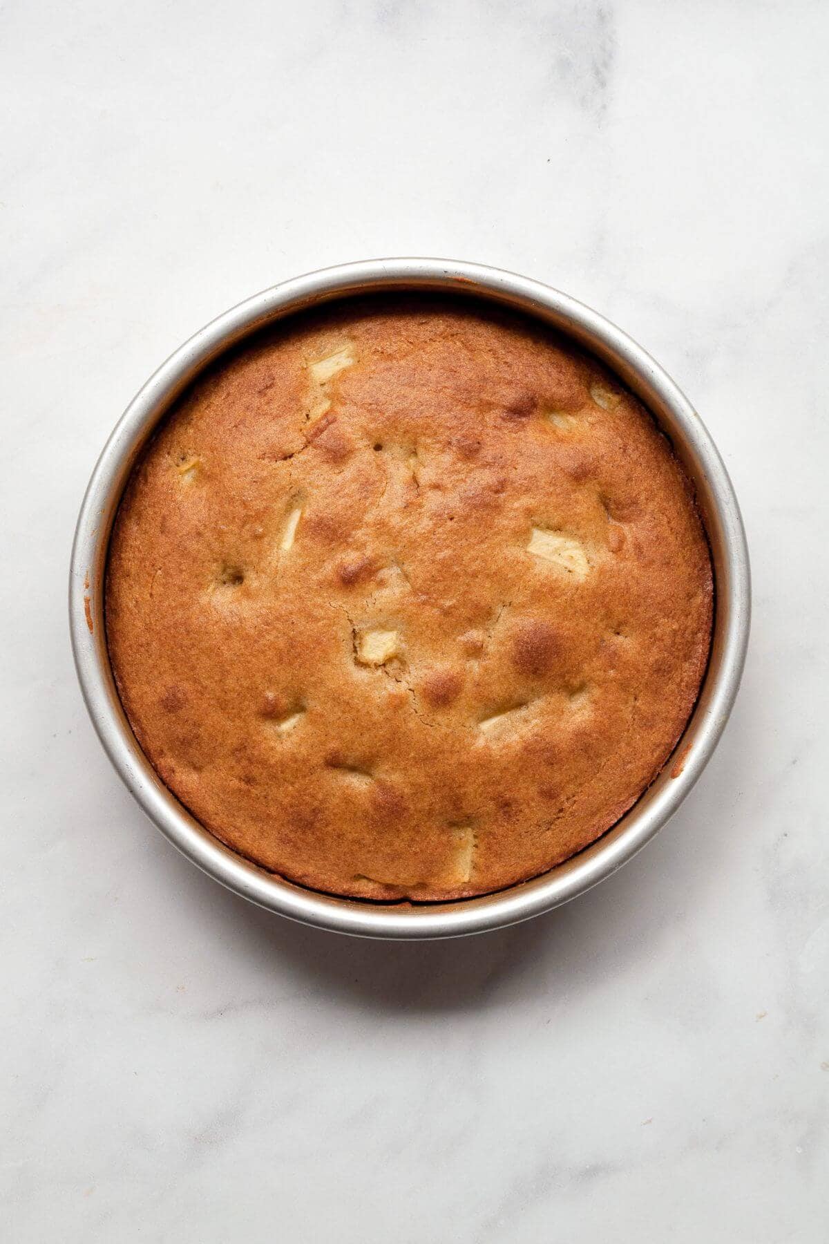 Freshly baked gluten-free apple cake in a cake pan with a golden top.