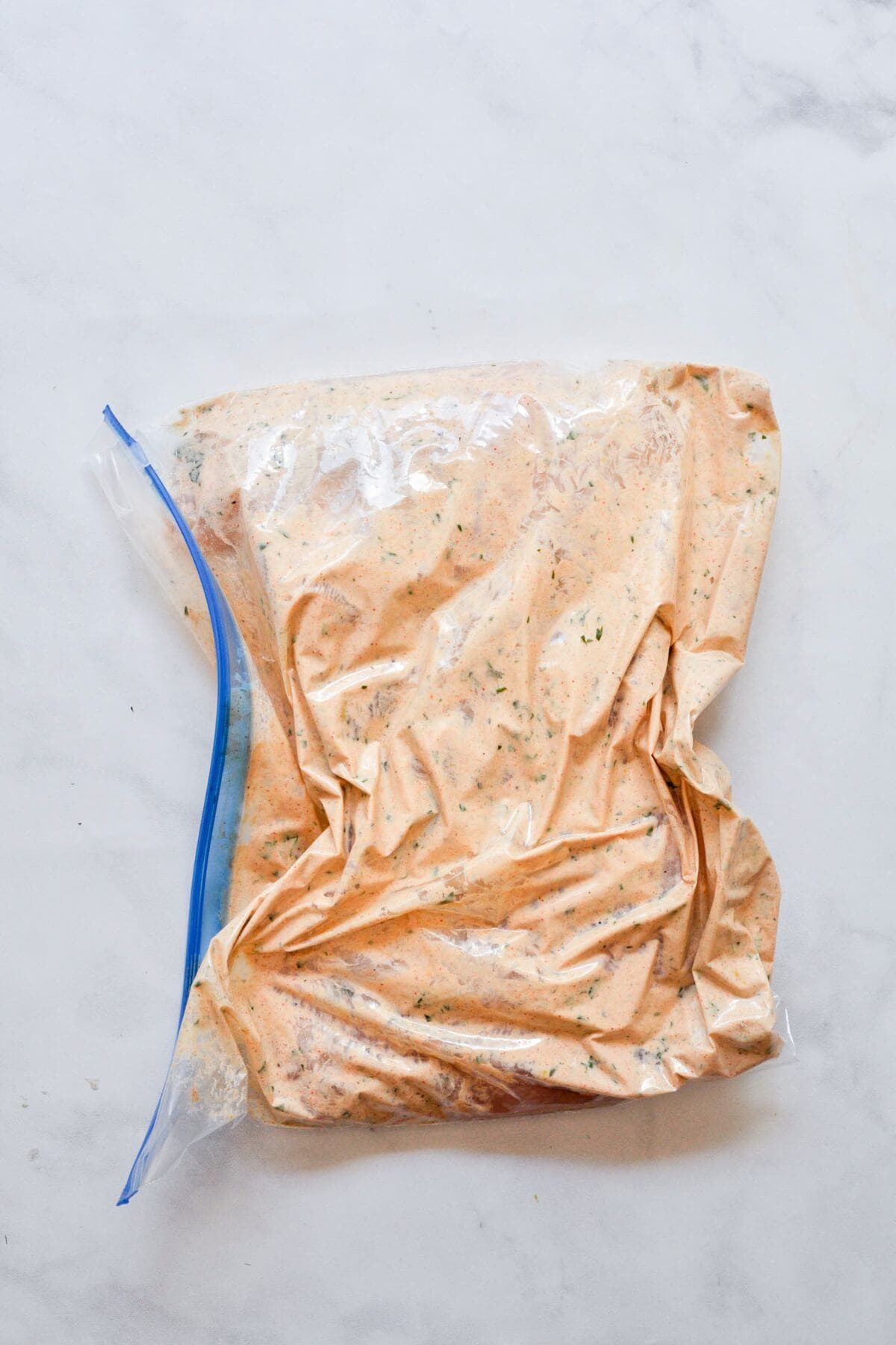 Chicken breasts marinating in Greek yogurt marinade in a zip-top bag.