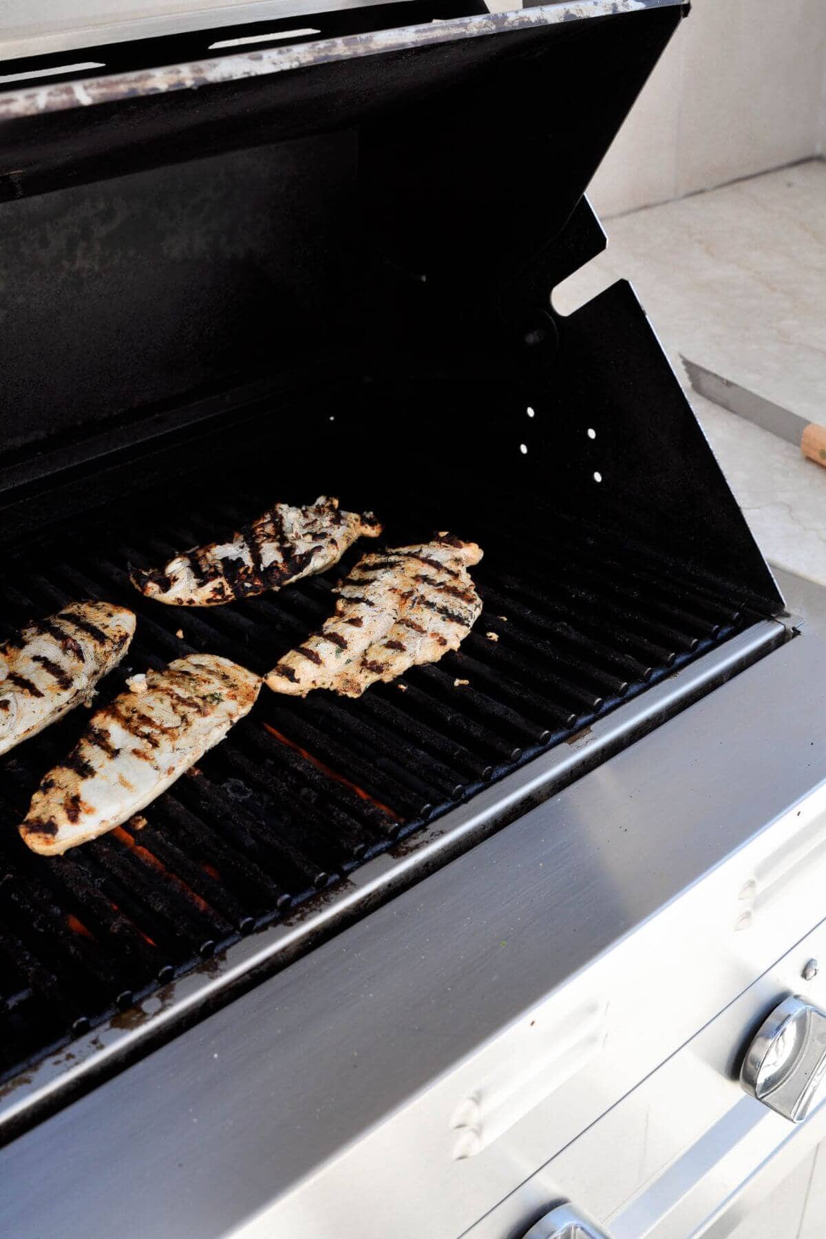Greek yogurt marinated chicken cooking on a grill.