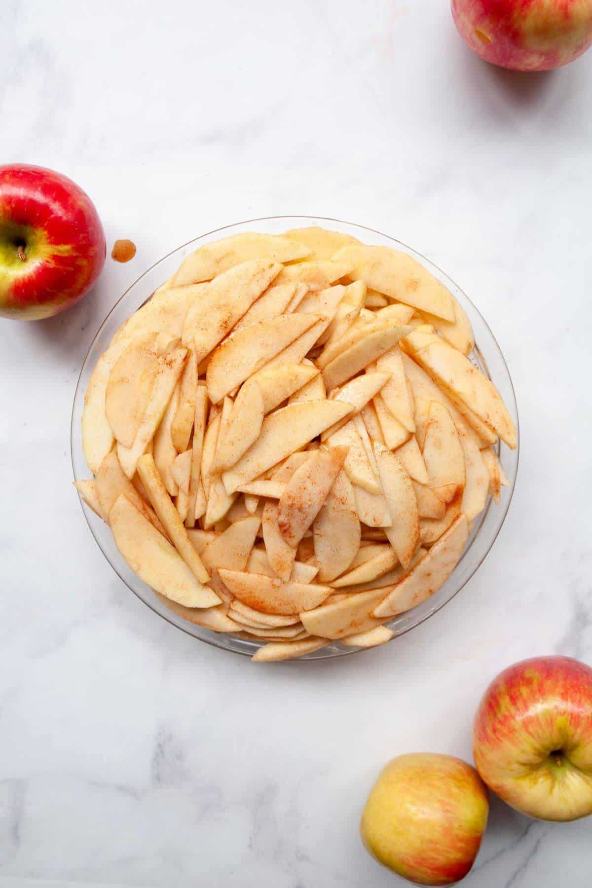 Apple crisp filling with sliced apples, maple syrup, cinnamon, and lemon in a pie dish before adding the crumble topping.