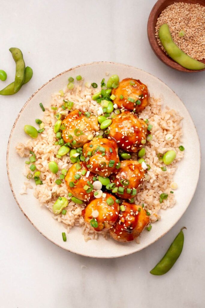 asian chicken meatballs on a plate with brown rice and edamame