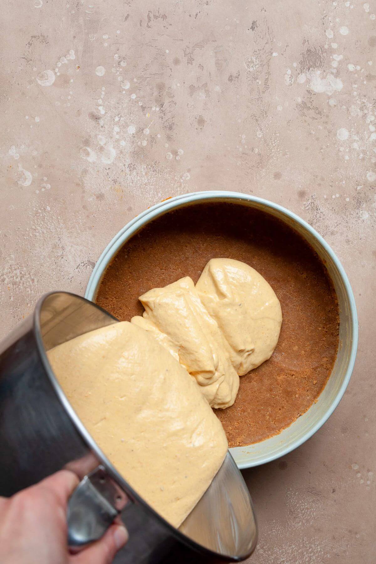 Pouring Greek yogurt pumpkin cheesecake batter onto the homemade gluten-free graham cracker crust.