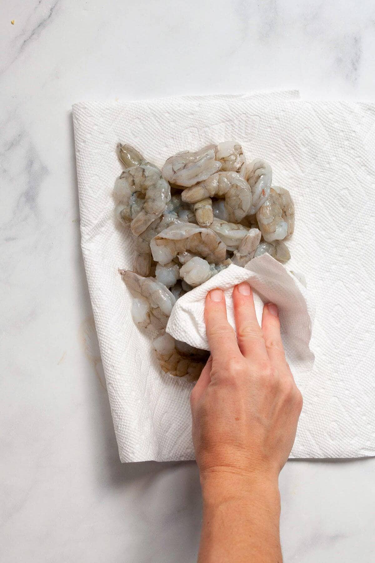 Hand patting raw shrimp dry with a paper towel.