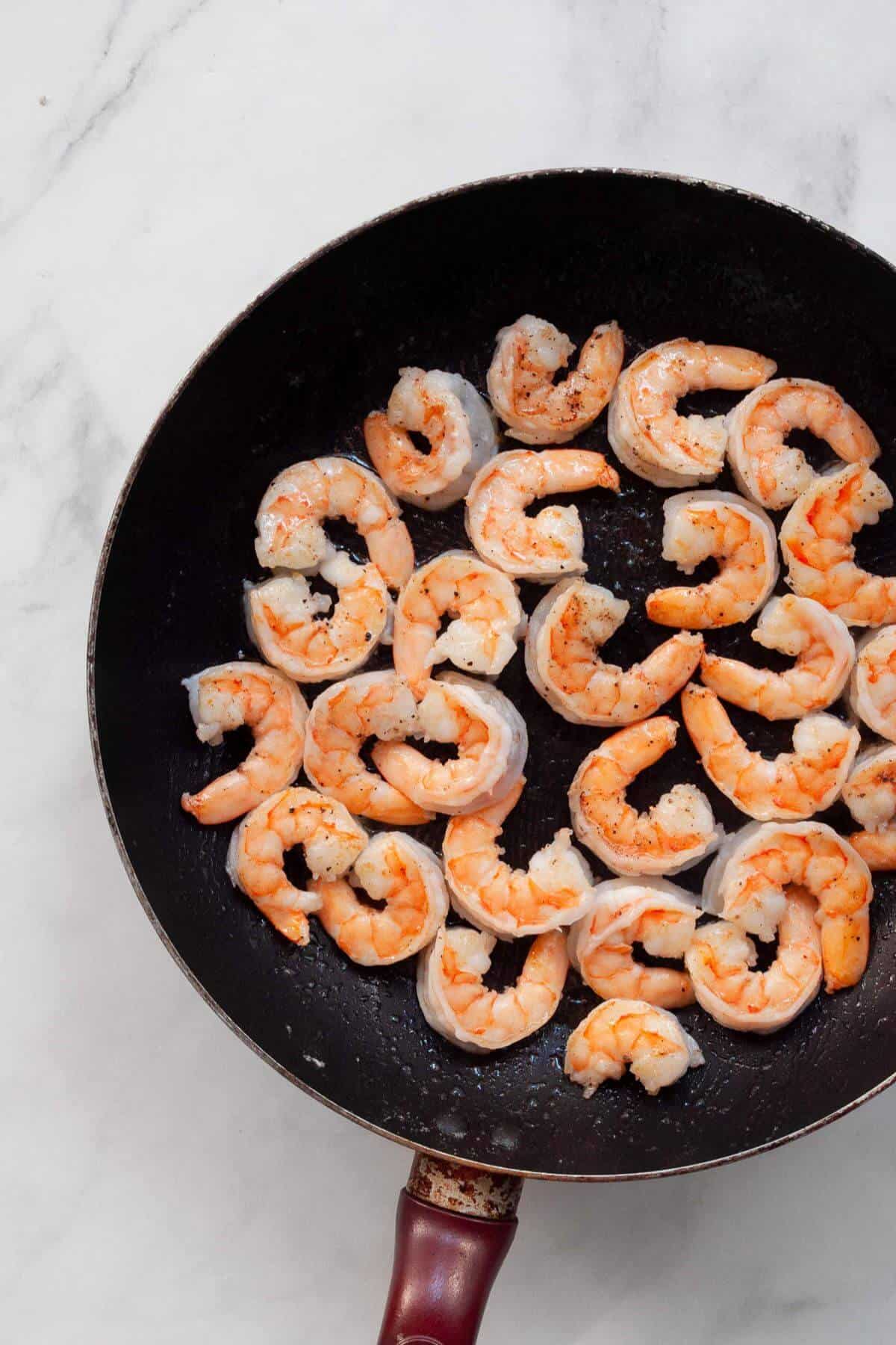 Shrimp sautéing in butter in a black skillet until pink.