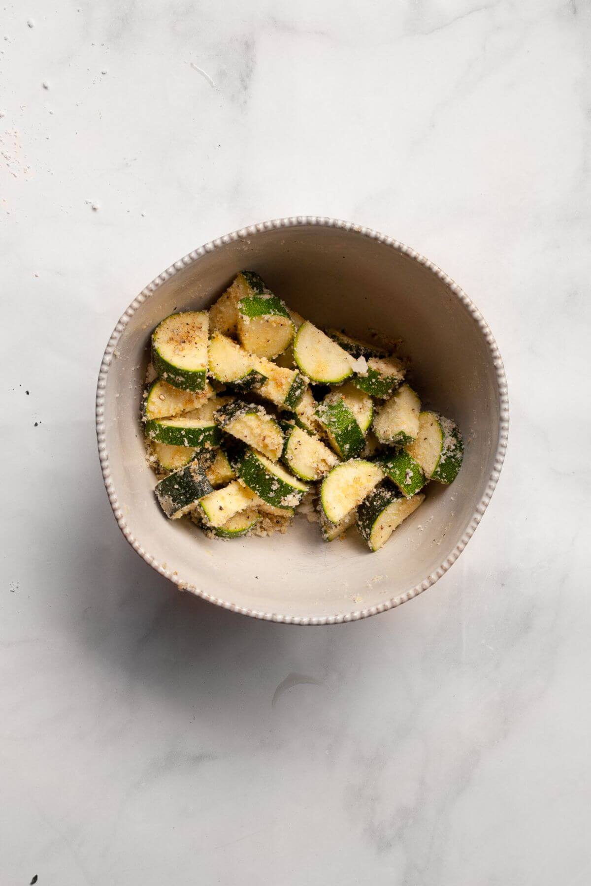 Bite-sized zucchini pieces in a mixing bowl tossed with Parmesan, garlic powder, onion powder, salt, and black pepper.