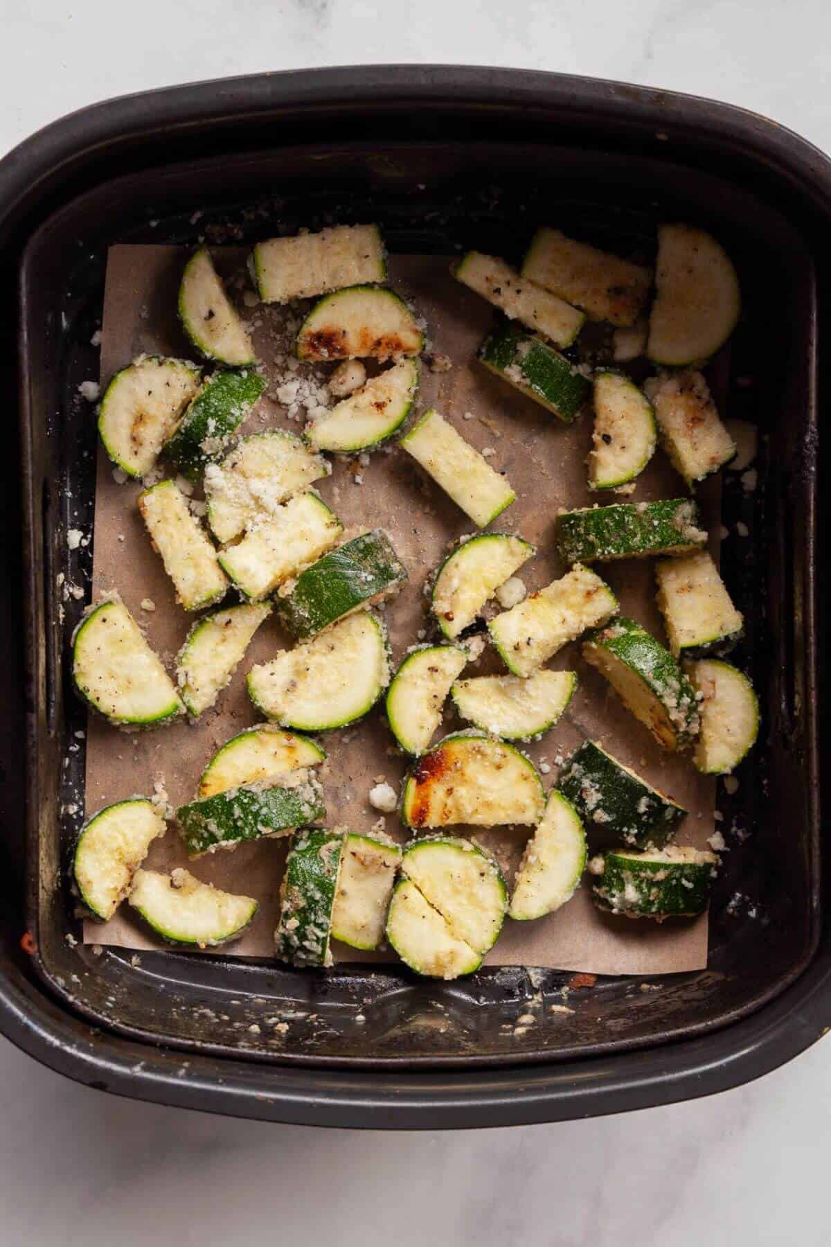 Parmesan garlic zucchini pieces arranged in a single layer in an air fryer basket with parchment paper before cooking.