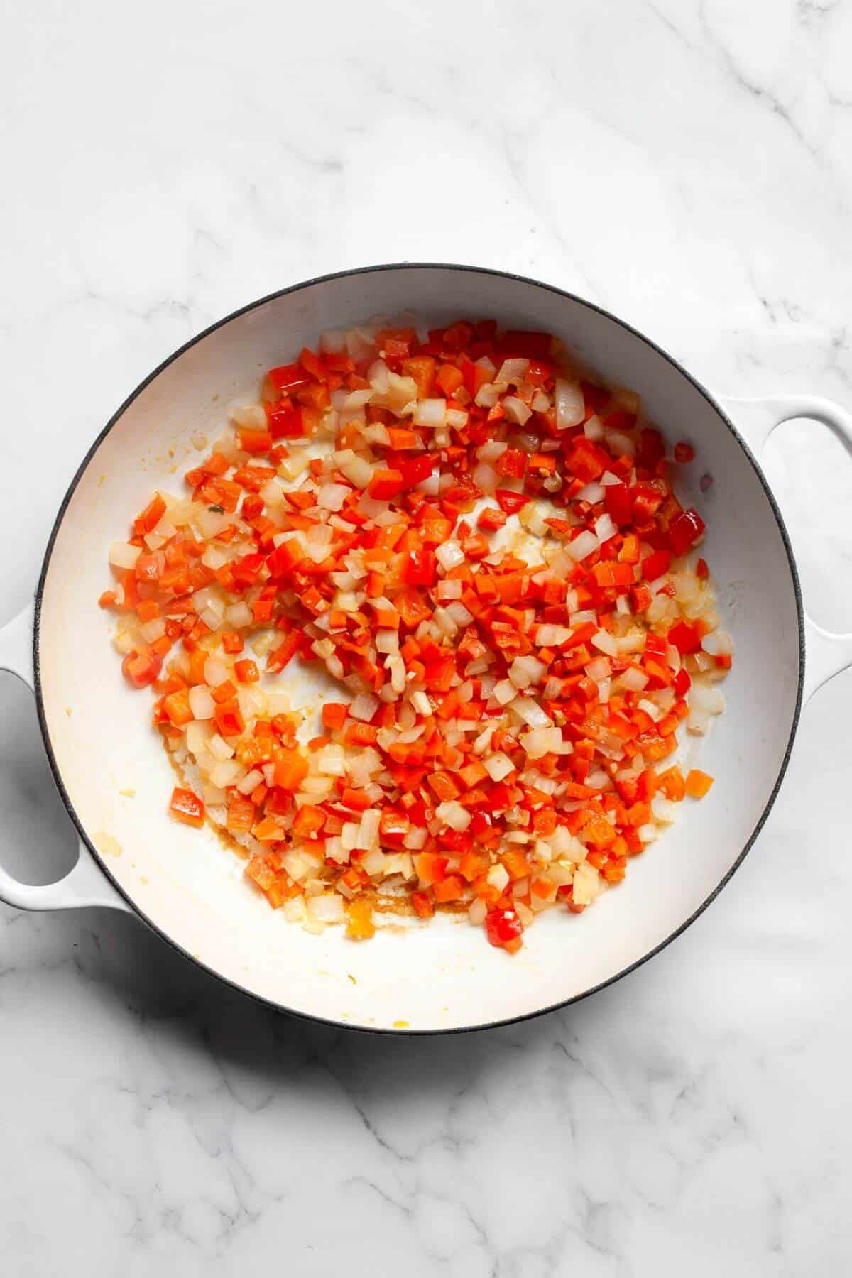 Diced onion, carrot, and red bell pepper sautéing in a white pan for healthy fried rice.