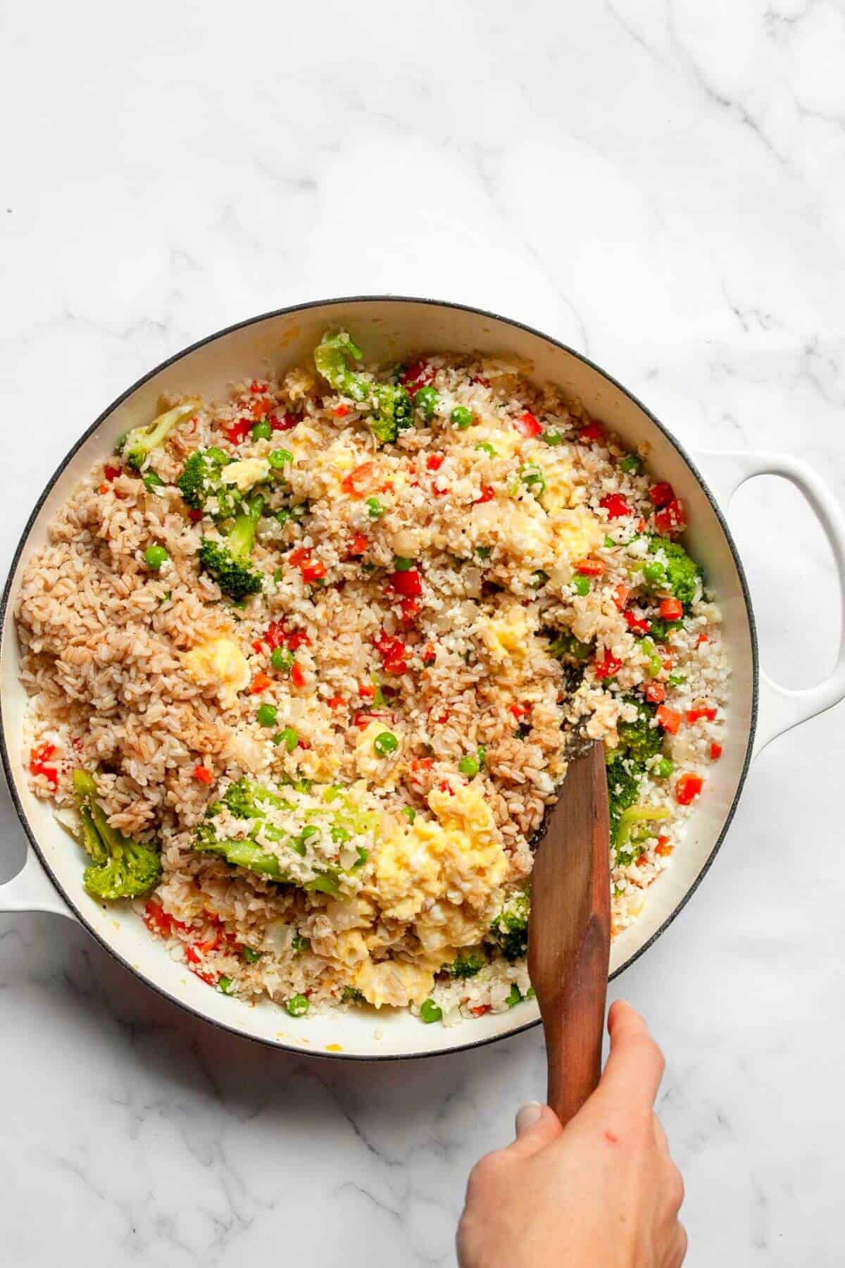 Scrambled eggs stirred into the vegetables and rice in the pan.