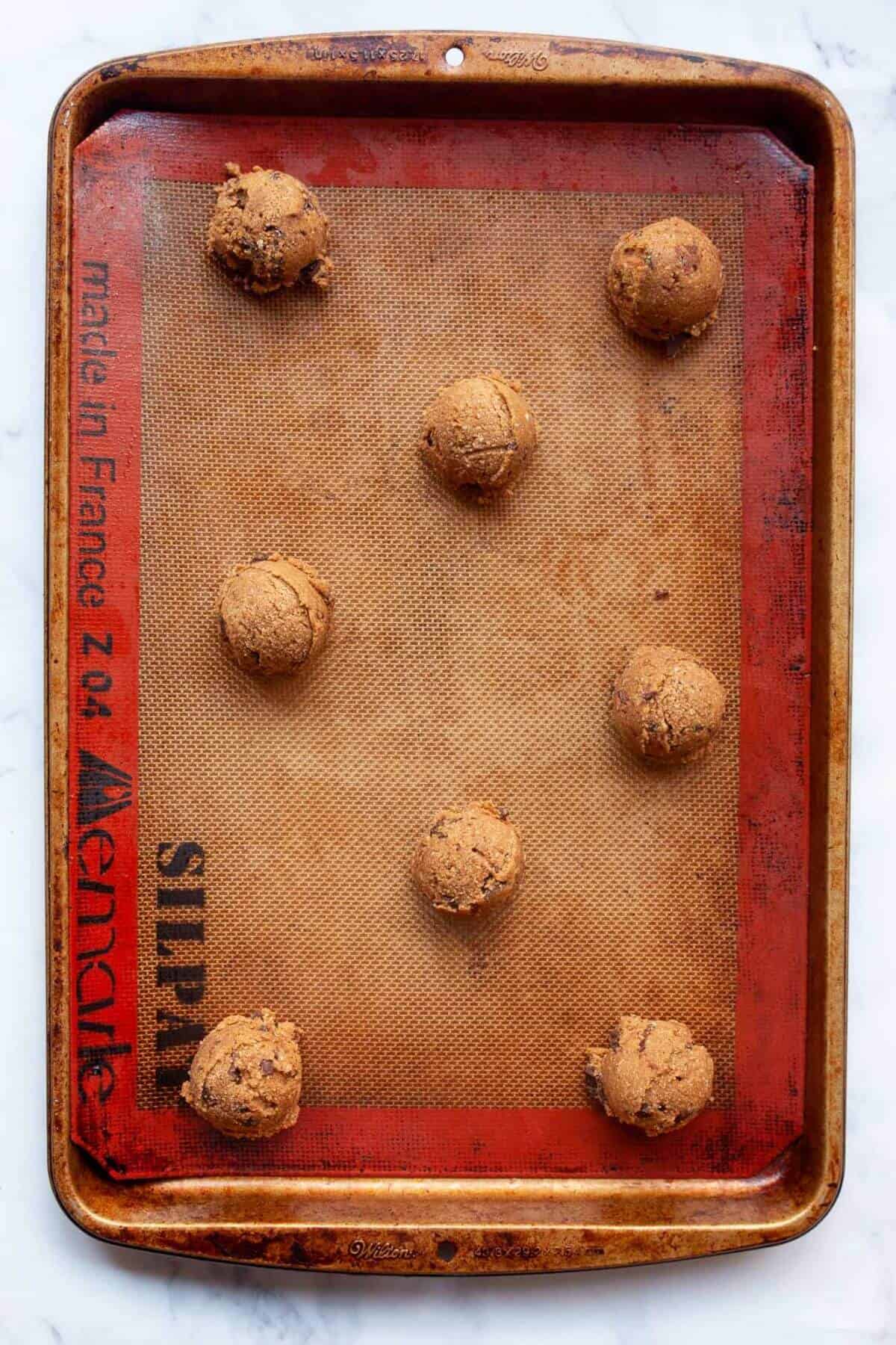 Unbaked oat flour chocolate chip cookie dough balls on a parchment-lined tray.