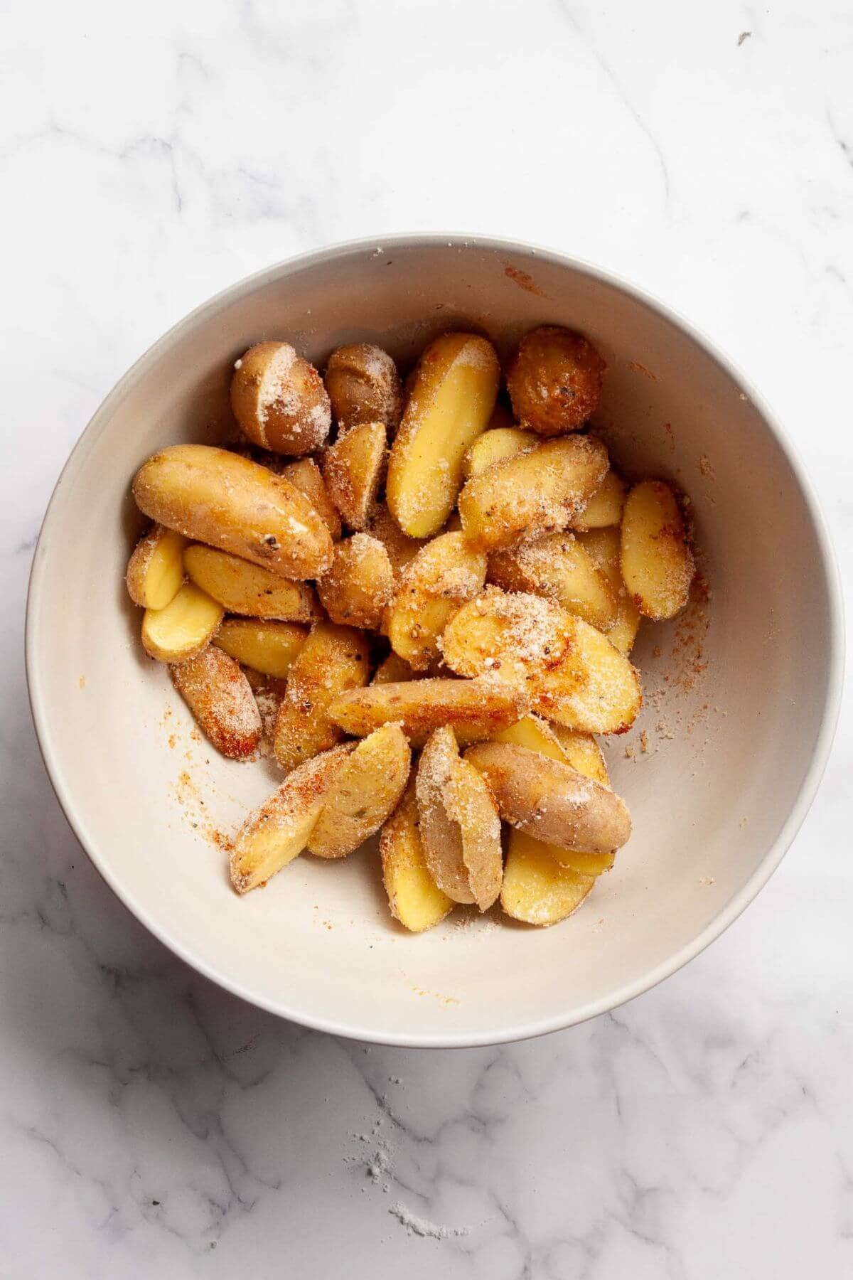 Raw cut fingerling potatoes in a mixing bowl with seasonings, olive oil, and parmesan cheese.