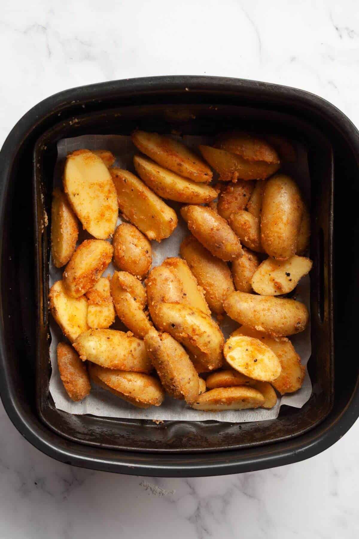 Uncooked seasoned fingerling potatoes in an air fryer basket.