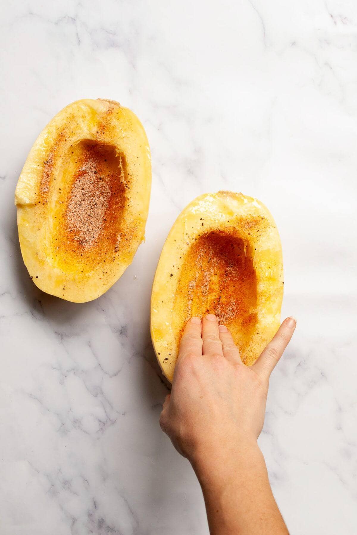 Seasoning spaghetti squash halves with olive oil, salt, pepper, paprika, onion powder, and garlic powder before cooking in the air fryer.