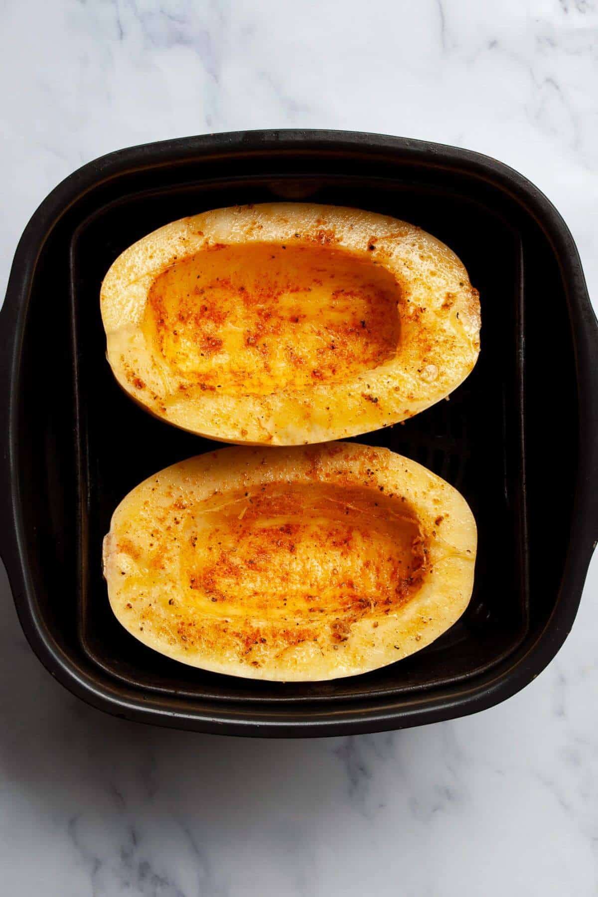 Seasoned spaghetti squash halves ready to cook in the air fryer basket.