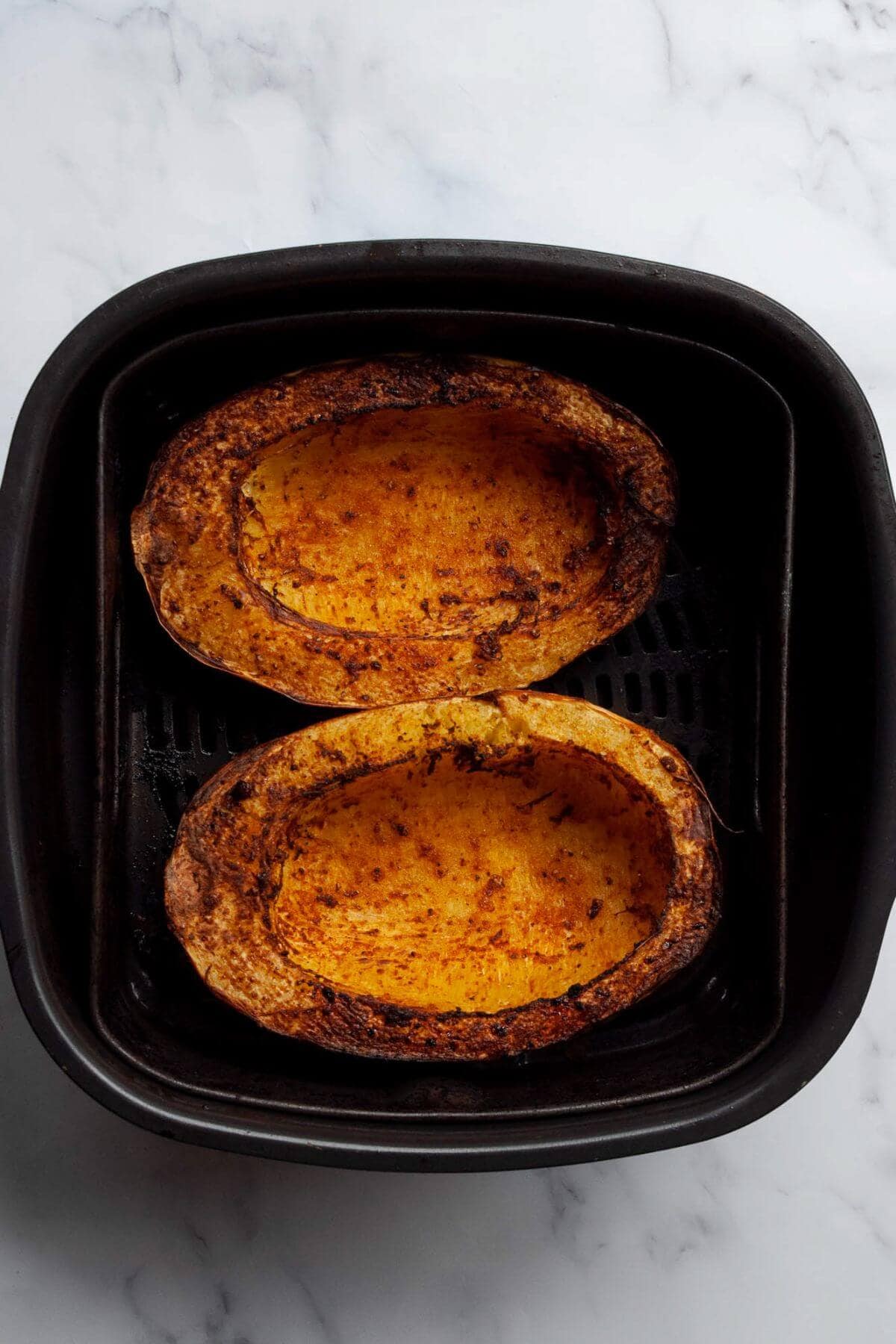 Two fork-tender, crispy cooked spaghetti squash halves sitting in an air fryer basket.