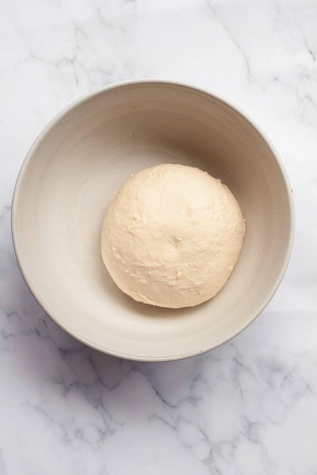 Smooth ball of kneaded bagel dough in a white mixing bowl.