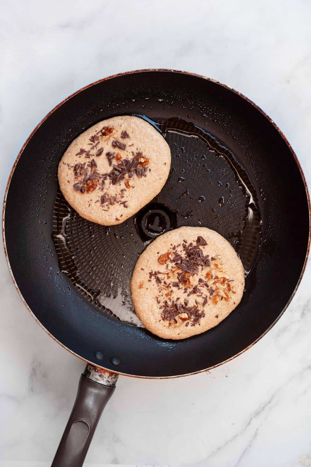 Cooking chocolate chip walnut banana pancakes in pan.