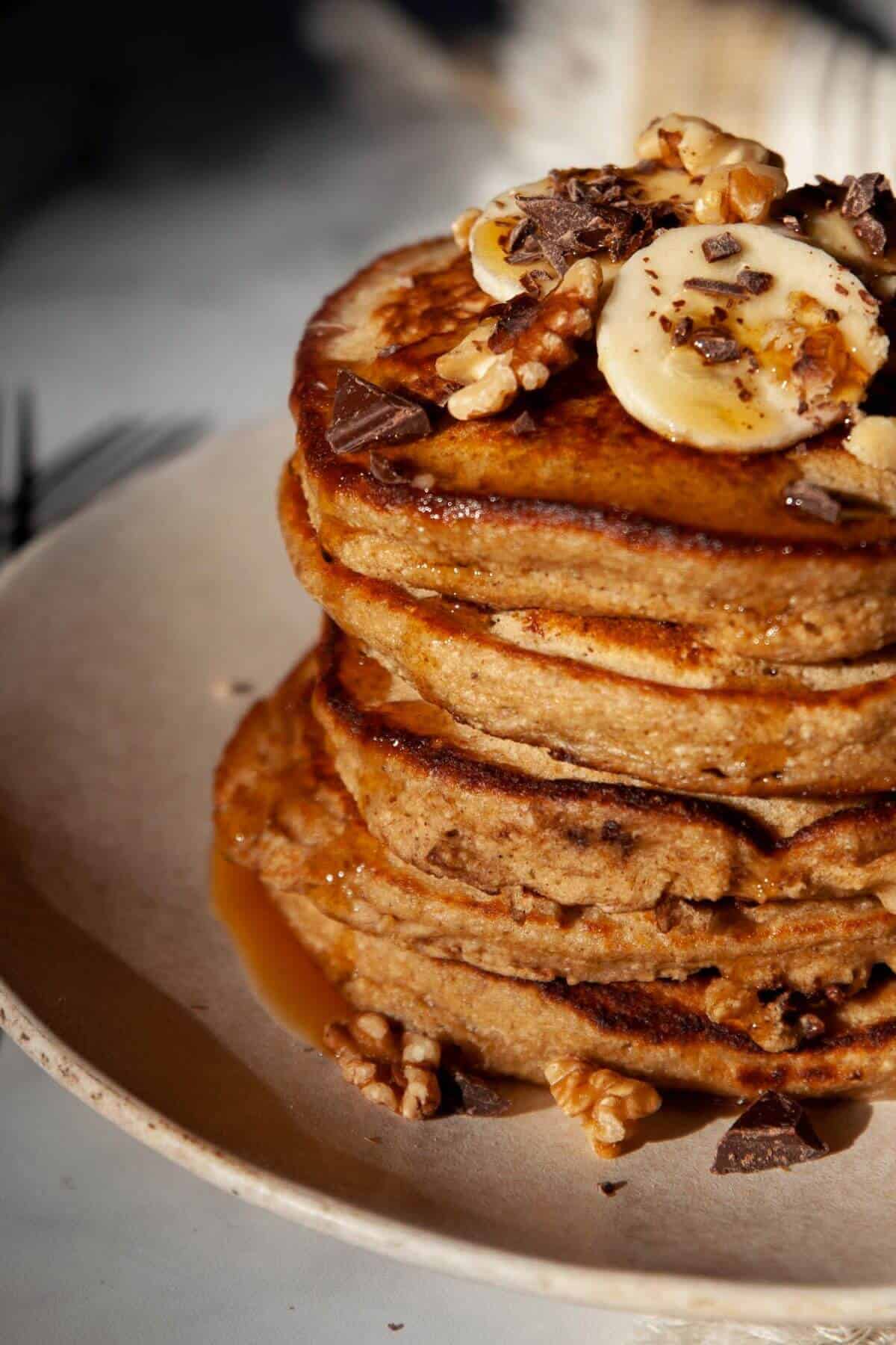 Stack of healthy oat flour chunky monkey banana pancakes with maple syrup on top and banana slices.