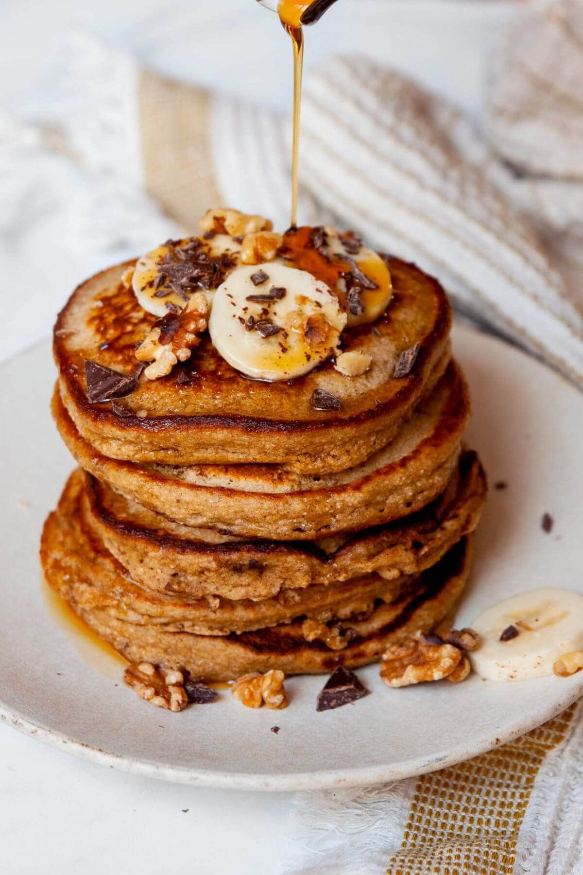 Pouring maple syrup on top of healthy oat flour chunky monkey banana pancakes.