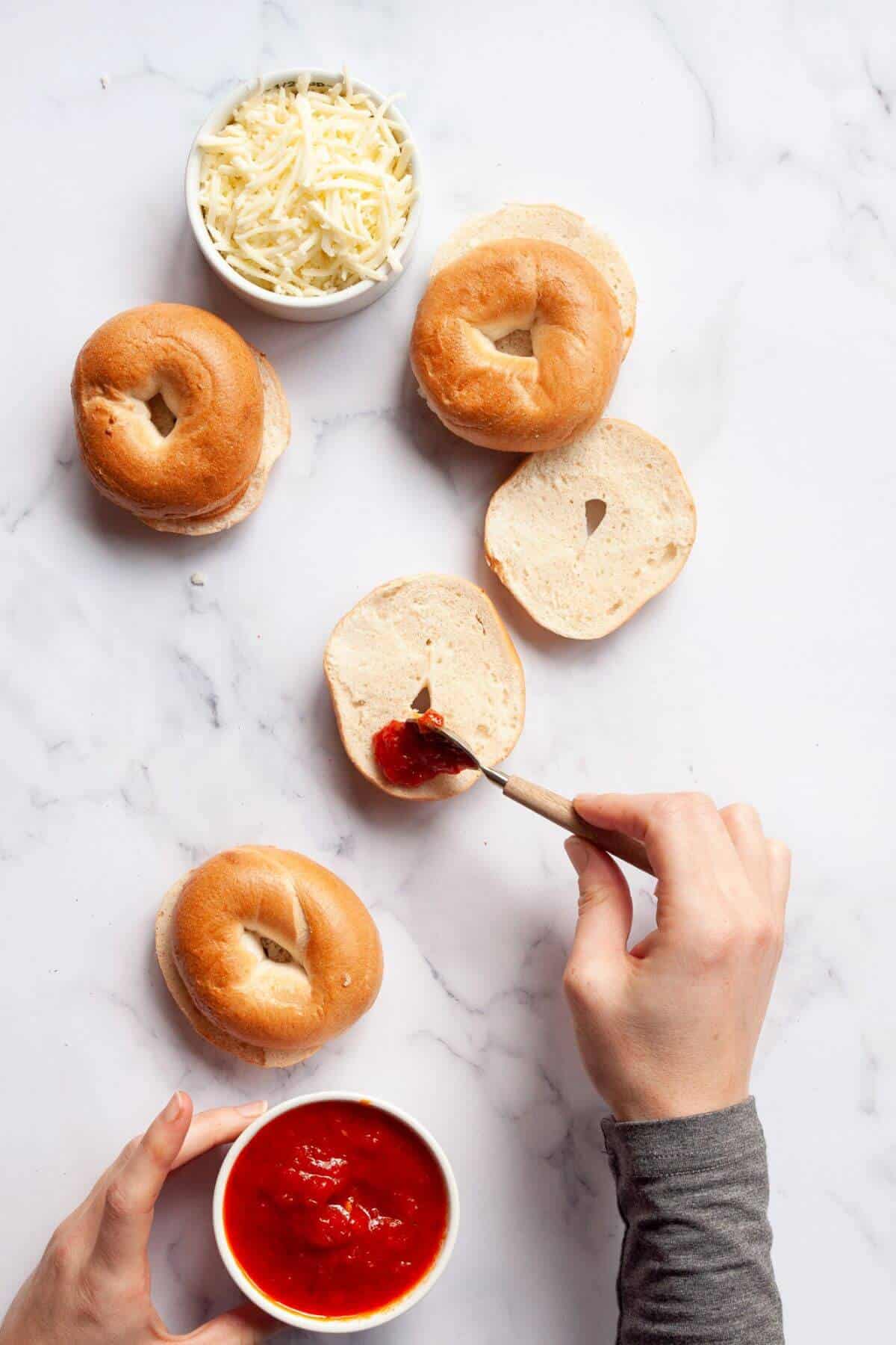 Spreading pizza sauce on halved mini bagels with a spoon.