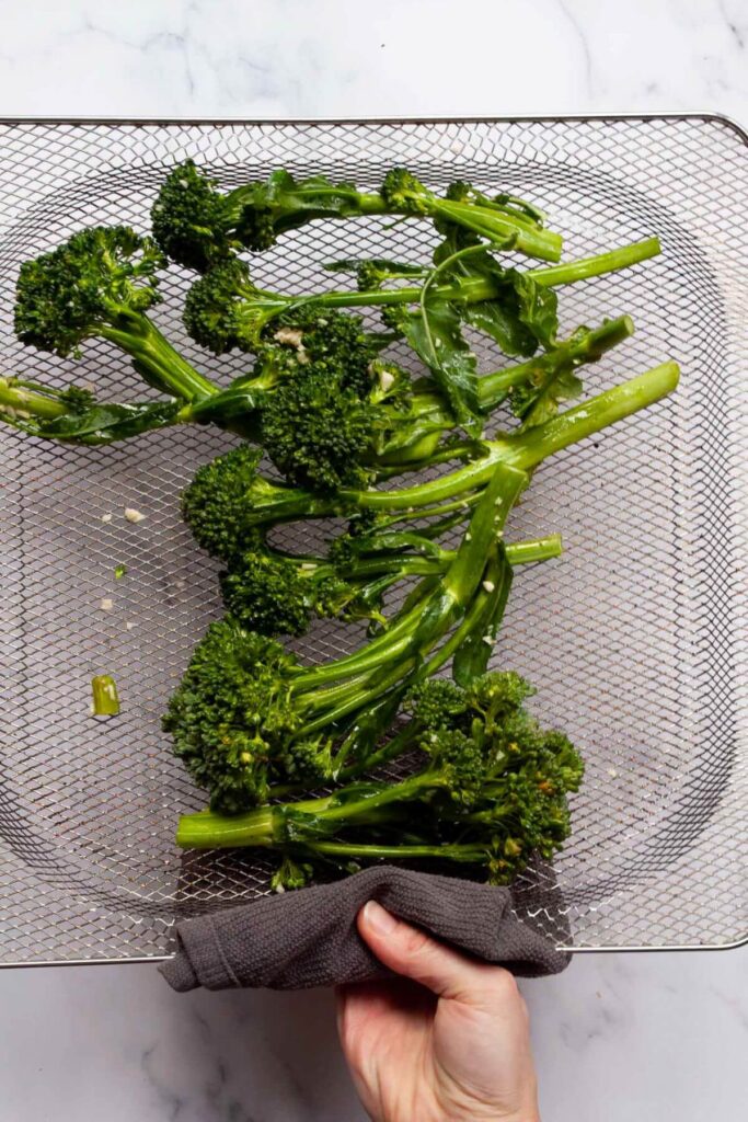 seasoned broccolini in air fryer basket before roasting