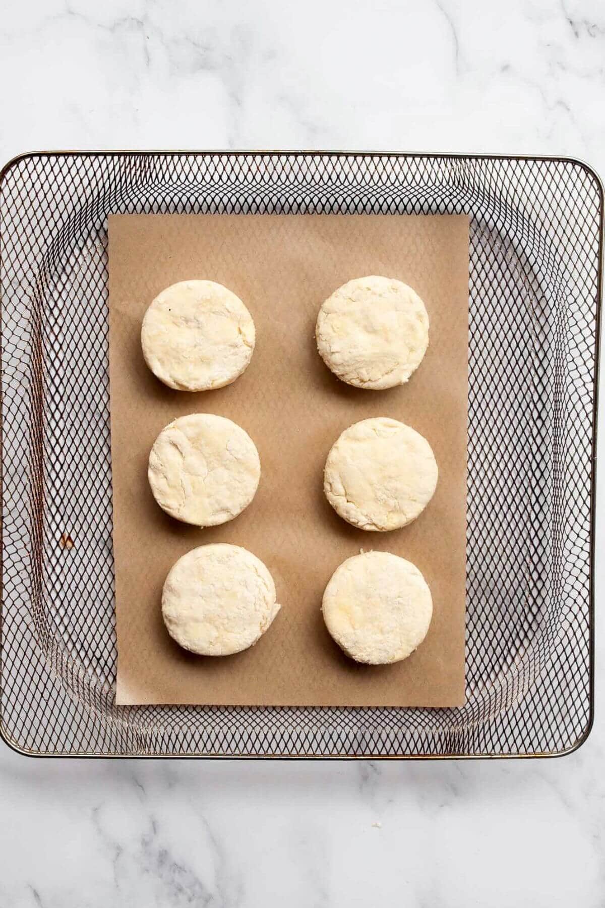 Raw biscuit rounds placed in air fryer basket with space between.