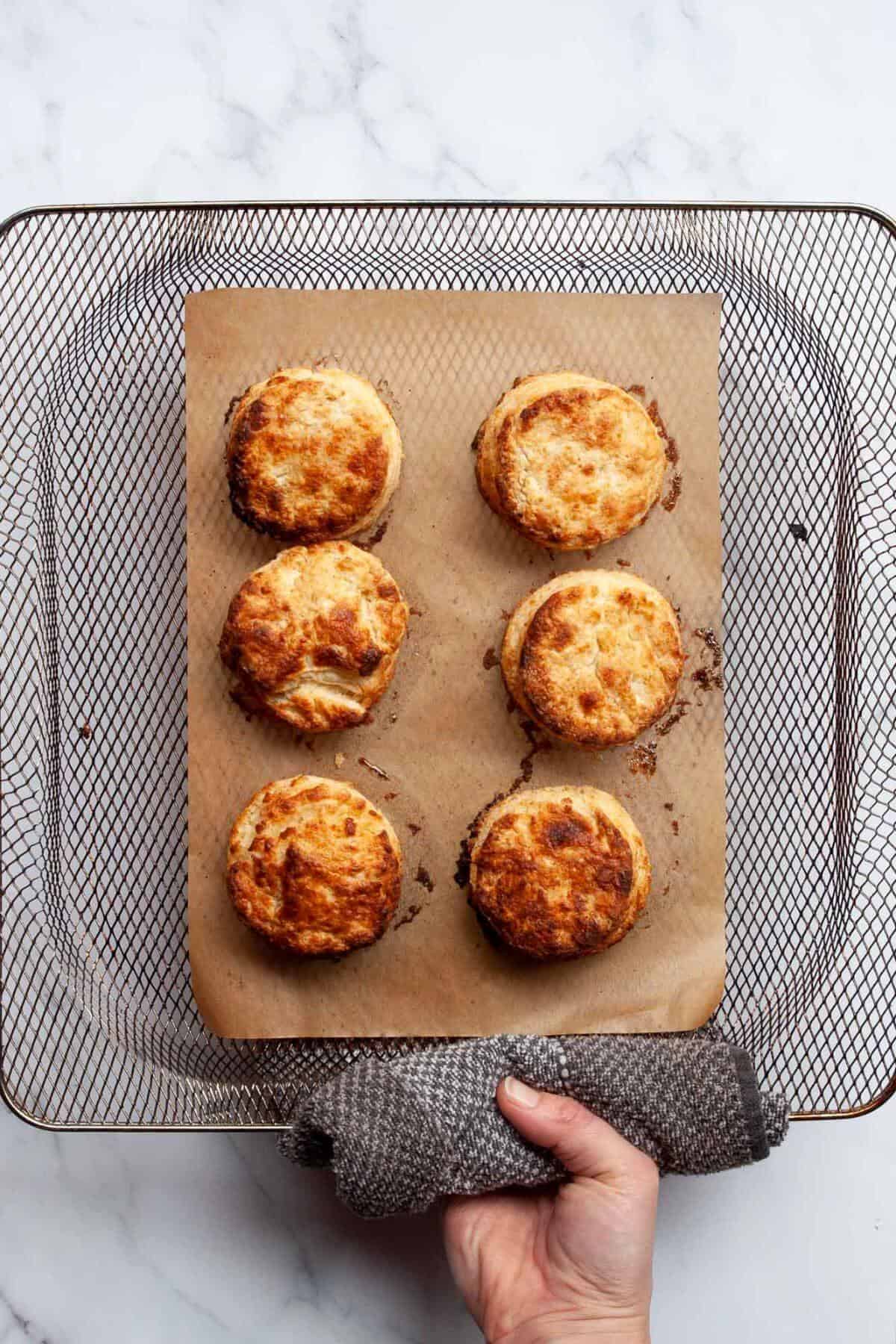 Biscuits cooking in air fryer basket until golden brown.
