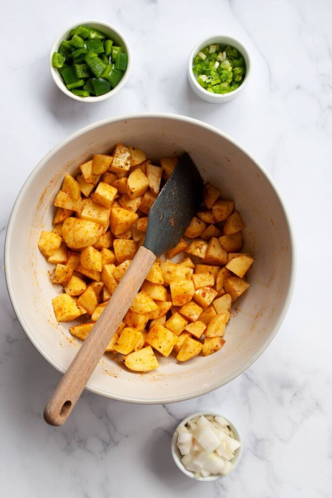 seasoning potatoes cubes with olive oil, salt, pepper, and paprika in a mixing bowl