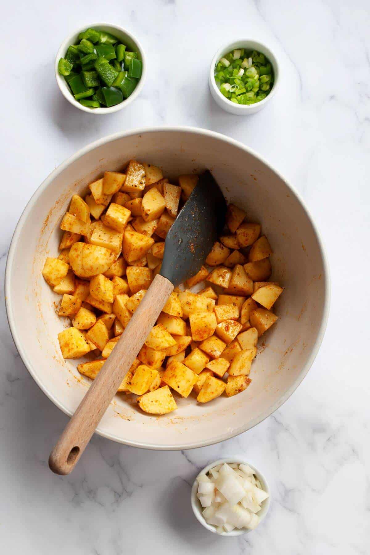 Seasoning 1-inch cut Yukon gold potatoes cubes with olive oil, salt, pepper, and paprika in a mixing bowl.