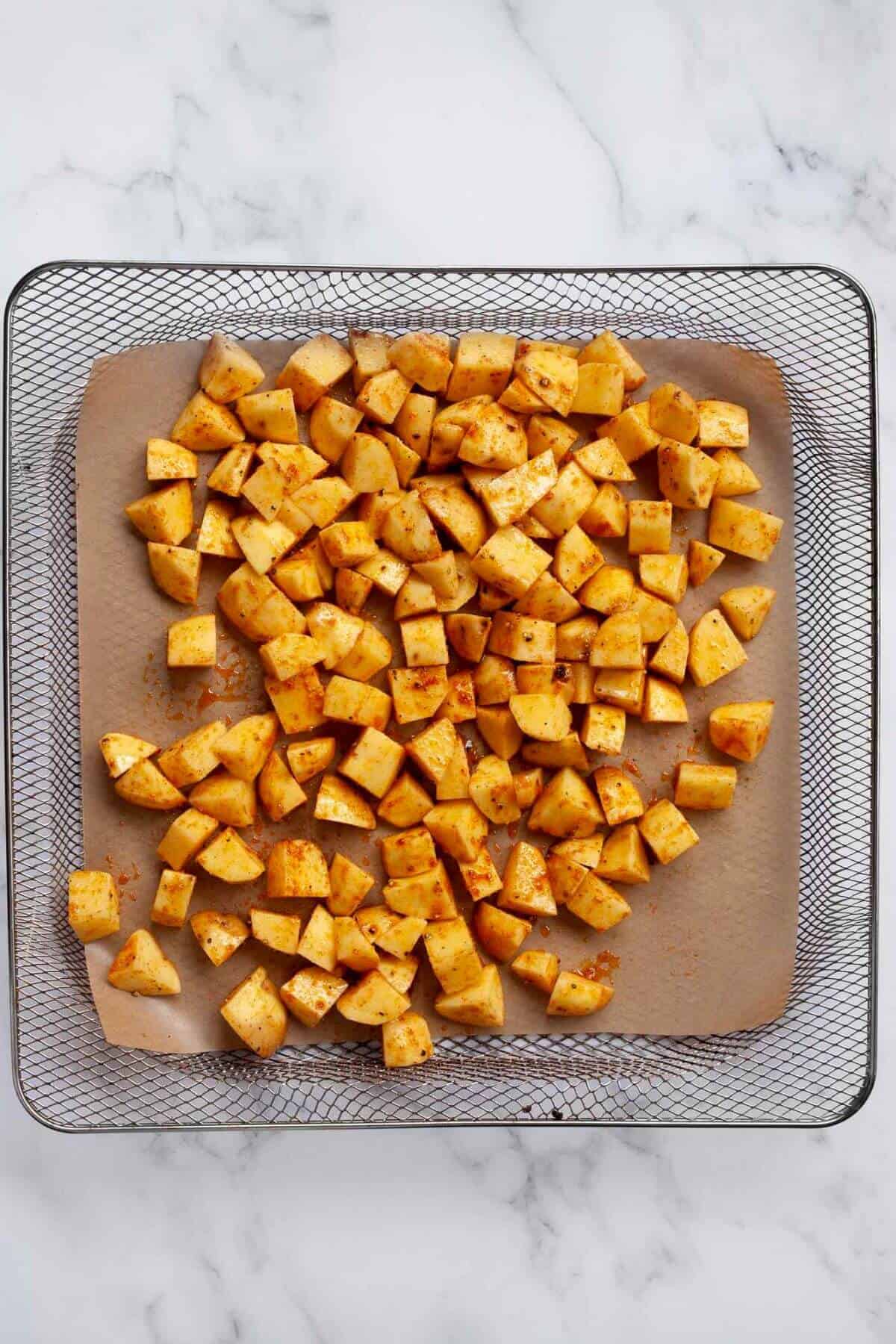Uncooked seasoned Yukon potato cubes in air fryer basket.