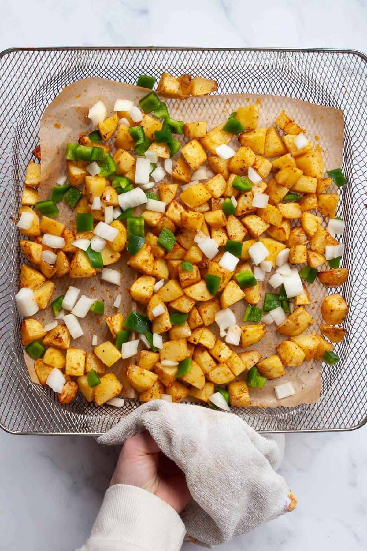 Adding chopped onions and green bell peppers to basket with air fried home fries.