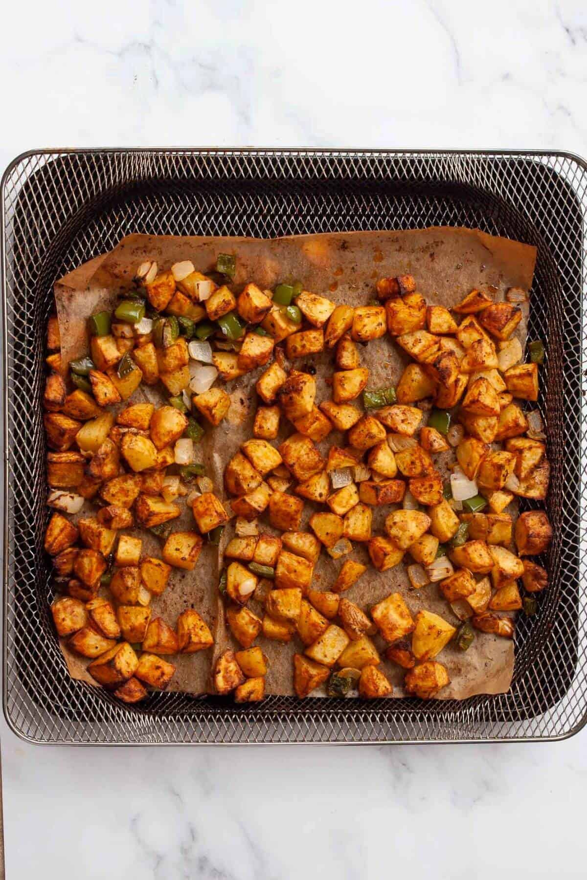 Extra crispy air fryer home fries with onions and peppers in basket.