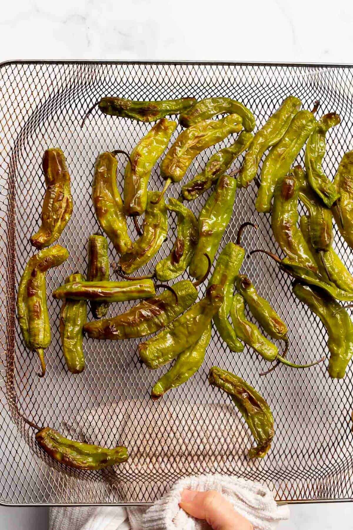 Blistered shishito peppers in air fryer basket after cooking.