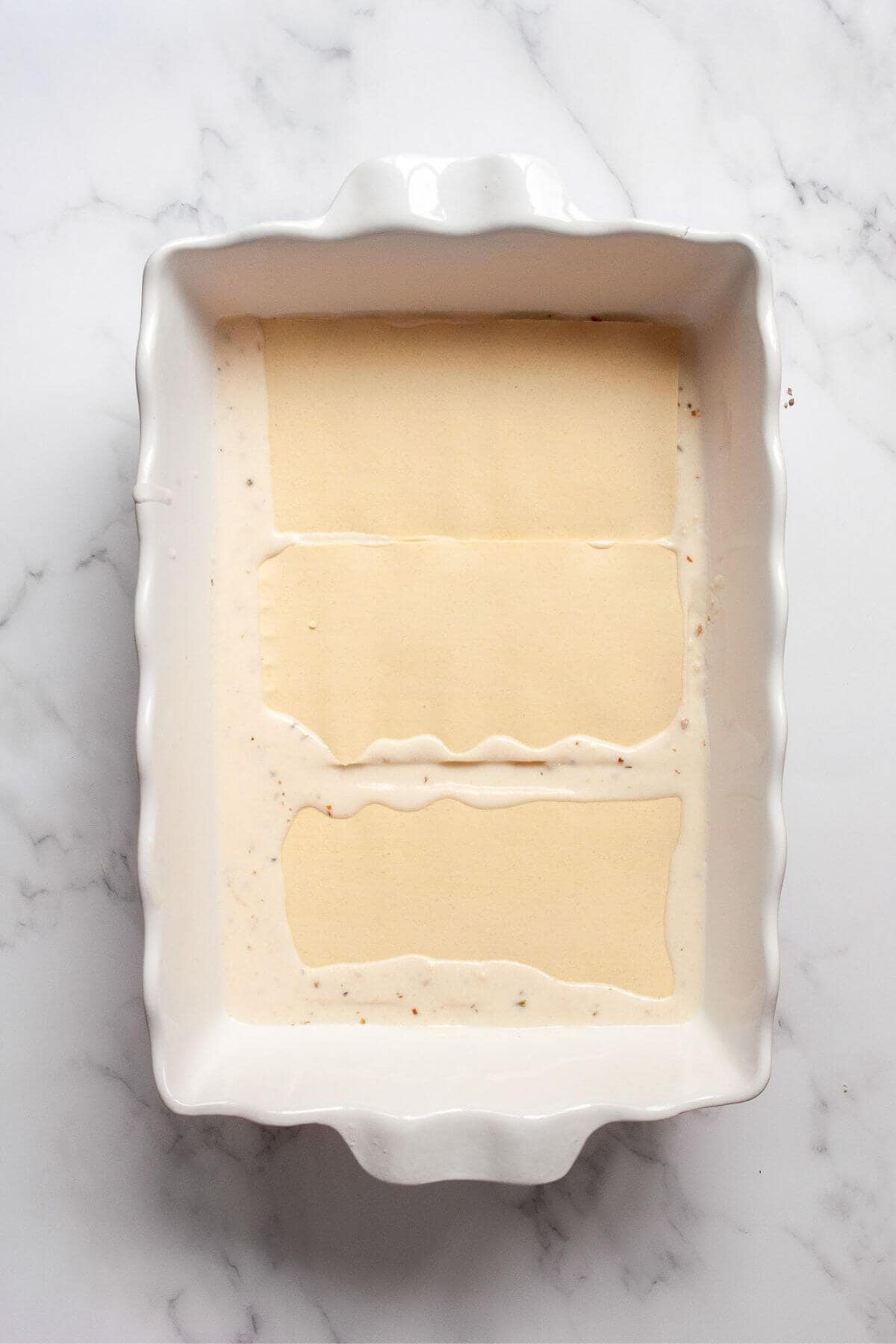 Adding lasagna noodles on top of creamy, lightened-up ricotta Alfredo sauce in a casserole dish while assembling chicken and broccoli lasagna.