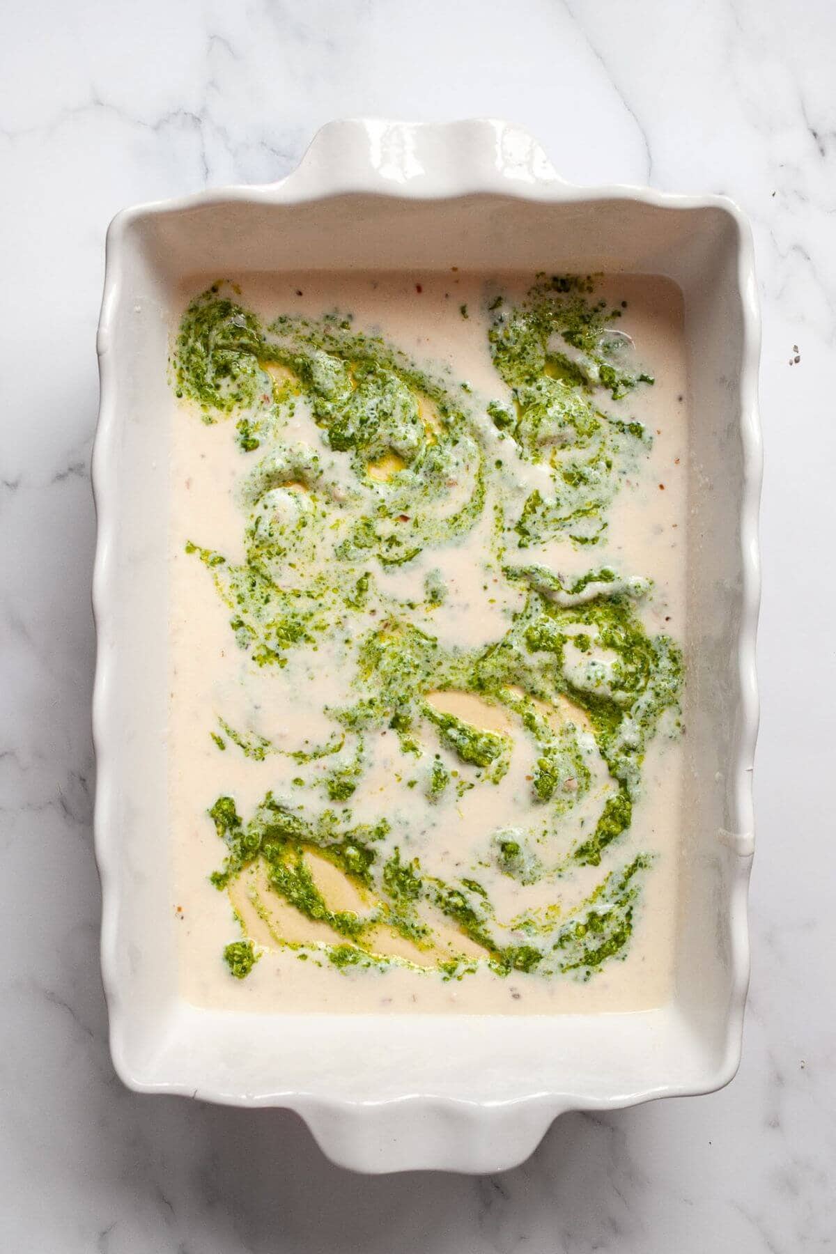 Spreading creamy ricotta white sauce and broccoli pesto over lasagna noodles while layering the chicken and broccoli lasagna Alfredo.