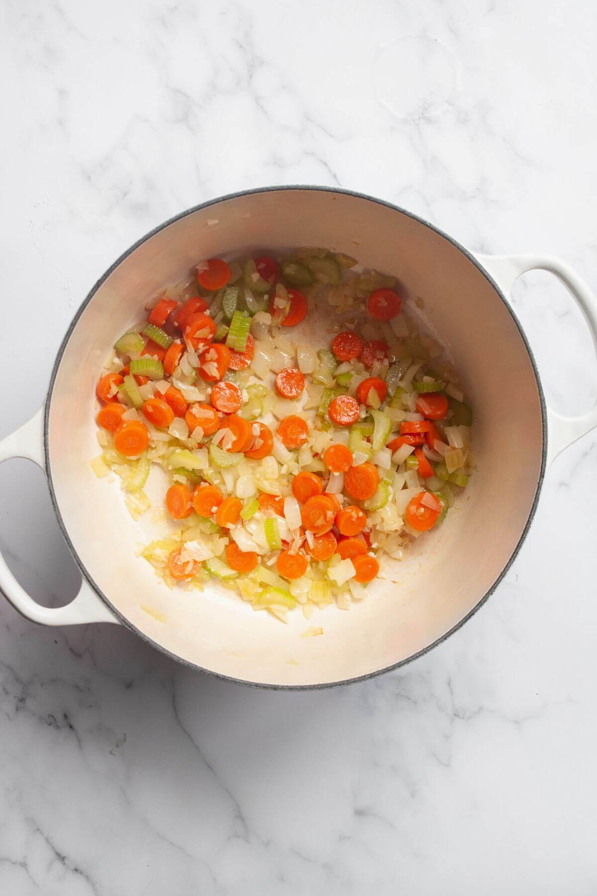Diced onion, carrots, and celery softening in butter in a white Dutch oven.