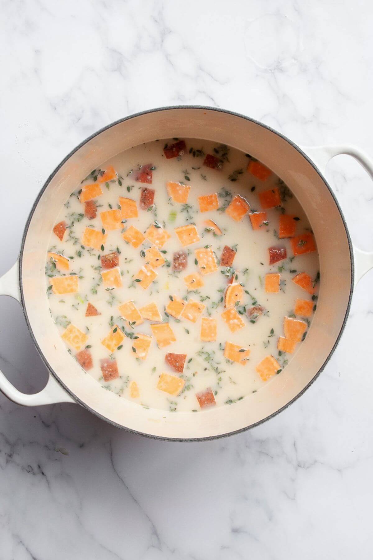 Sweet potato cubes simmering in chicken broth and milk in a Dutch oven.