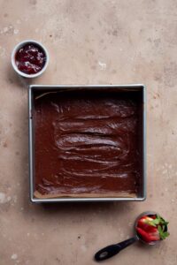brownie batter in a baking pan before swirling in strawberry preserves and topping with fresh strawberries