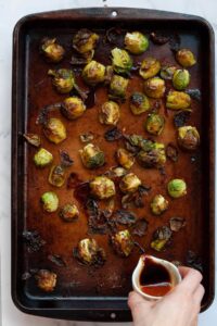 pouring the balsamic maple glaze on top of the crispy roasted brussle sprouts