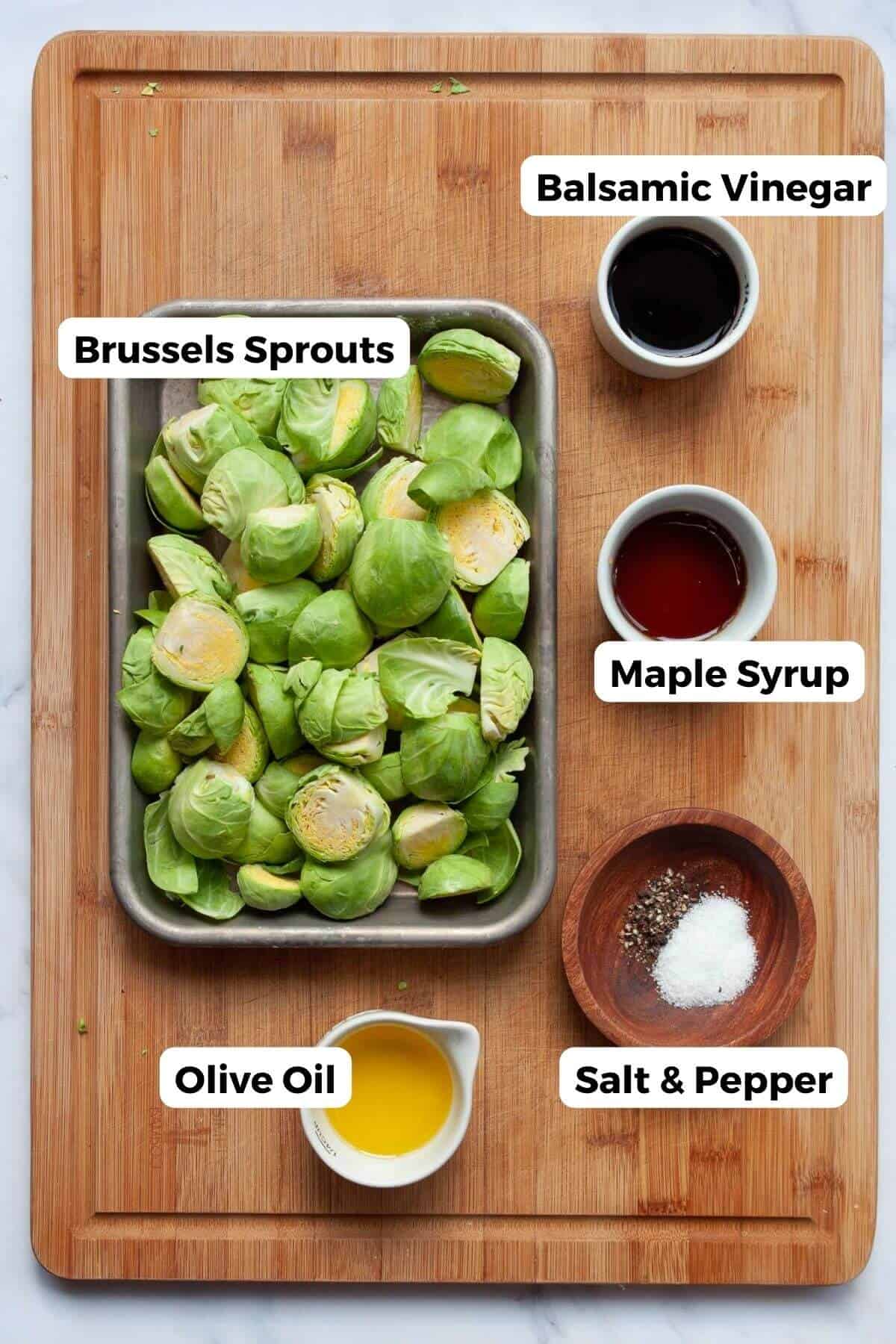All ingredients in the recipe in small bowls with labels, including: raw Brussels sprouts, balsamic vinegar, maple syrup, salt, pepper, and olive oil.