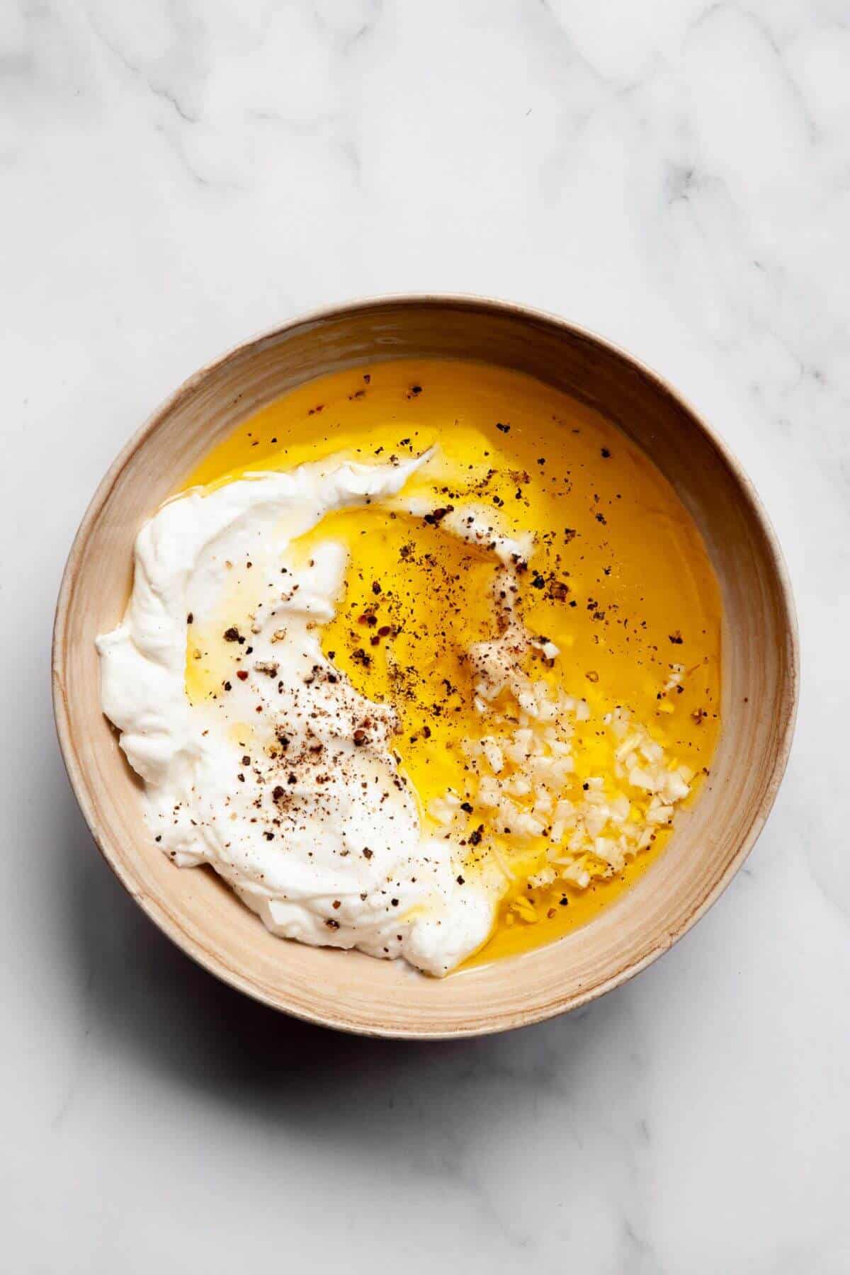 All the ingredients for healthy Greek yogurt Caesar dressing in a mixing bowl before whisking — Greek yogurt, lemon juice, Dijon mustard, garlic, olive oil, and pickle juice.