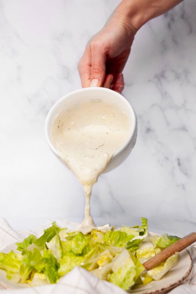 drizzling caesar salad dressing without anchovies on a salad