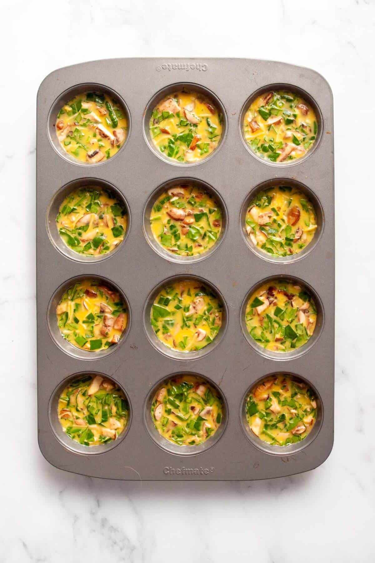 Muffin tin filled with keto egg bite batter with mix-ins before baking.