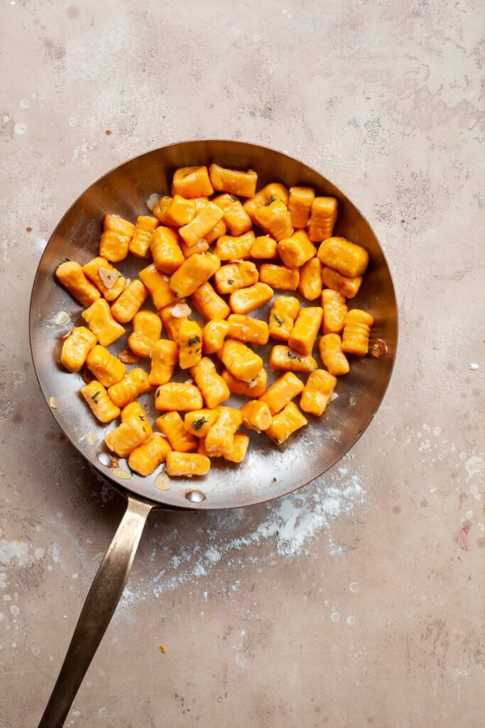 tossing cooked sweet potato gnocchi in homemade garlic butter sauce in a pan