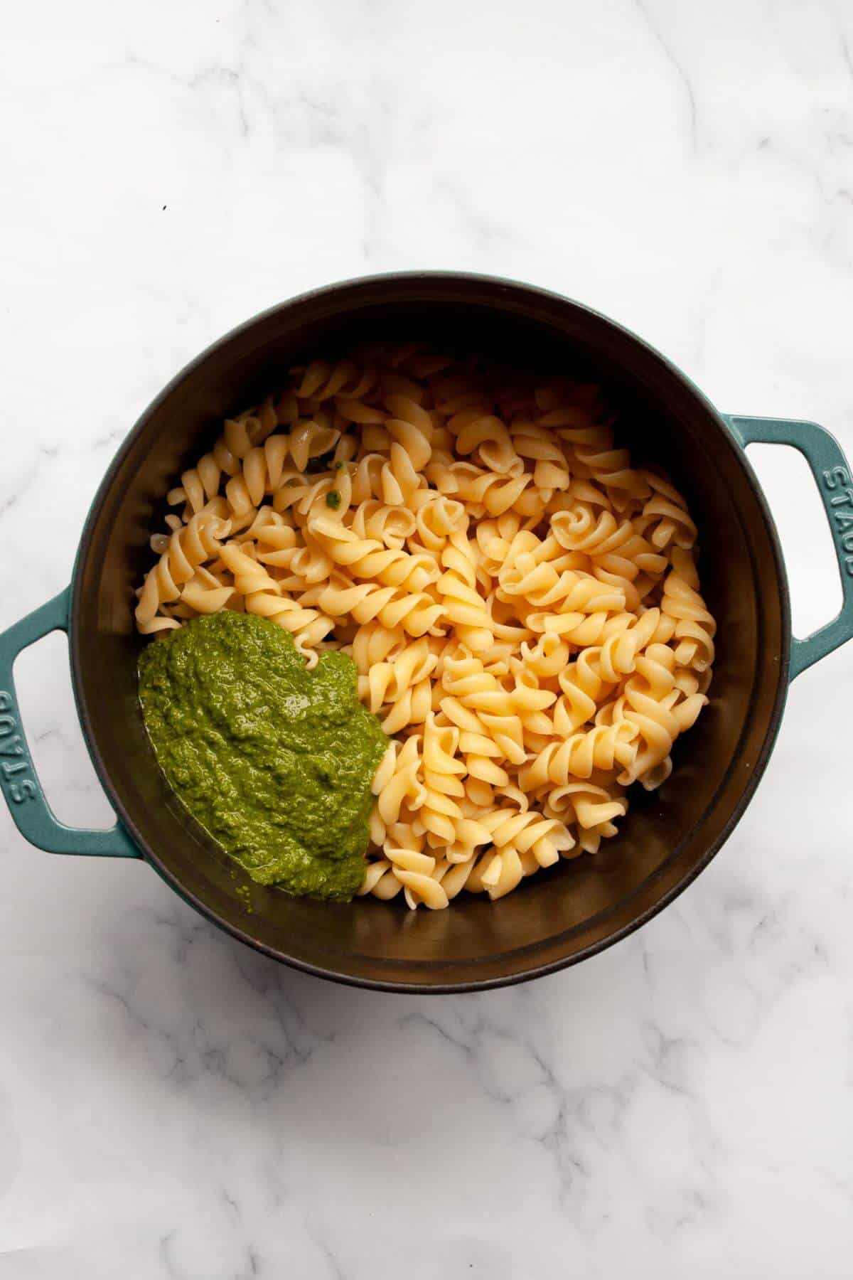 Basil pesto spooned over cooked fusilli in a green pot.