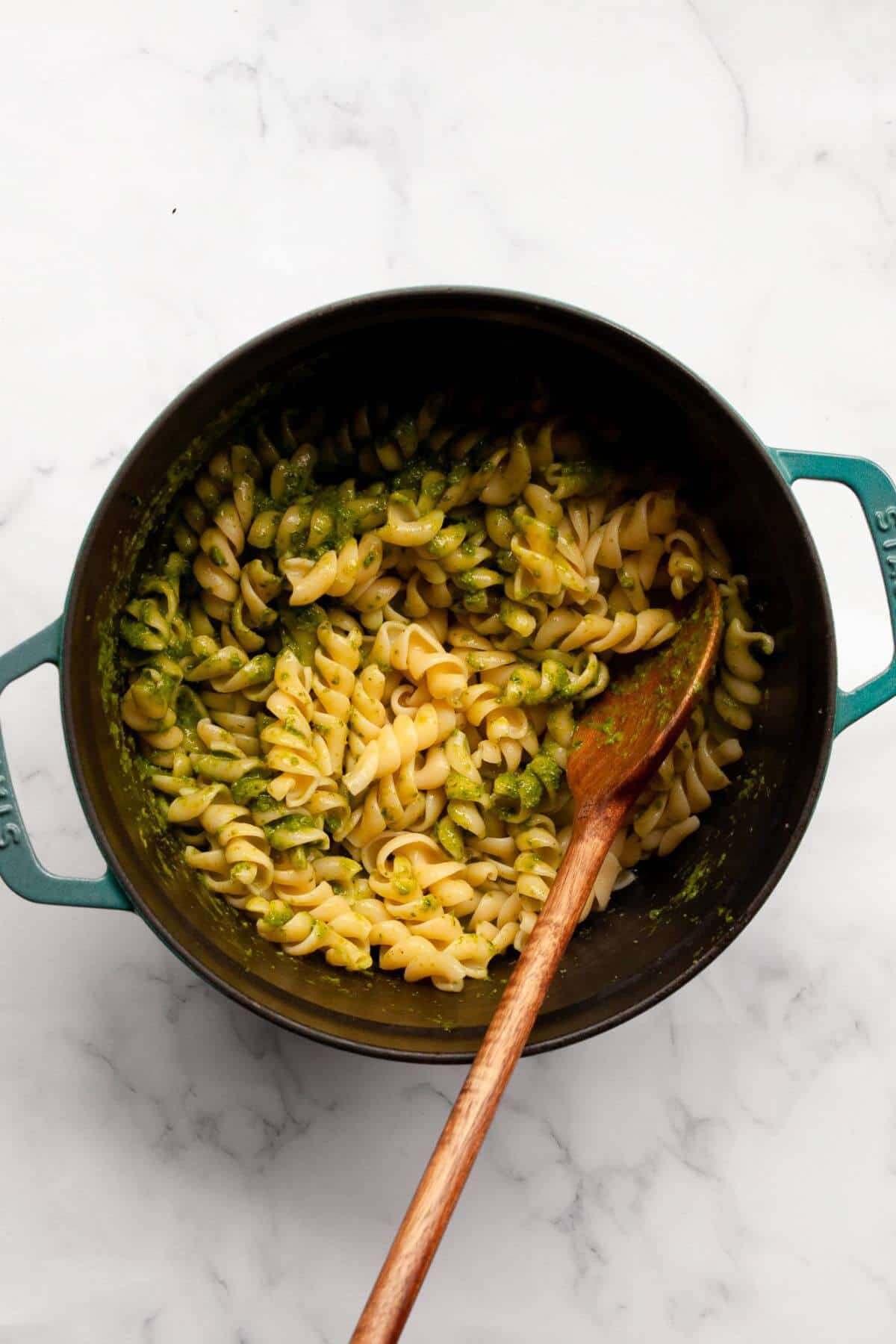Fusilli tossed with pesto sauce in a pot with a wooden spoon.