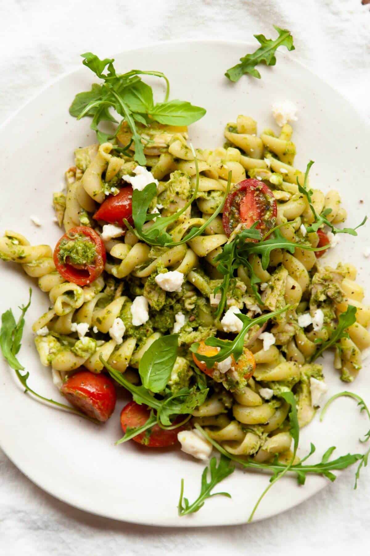 Cold tuna pesto pasta salad with arugula and cherry tomatoes on a white plate.