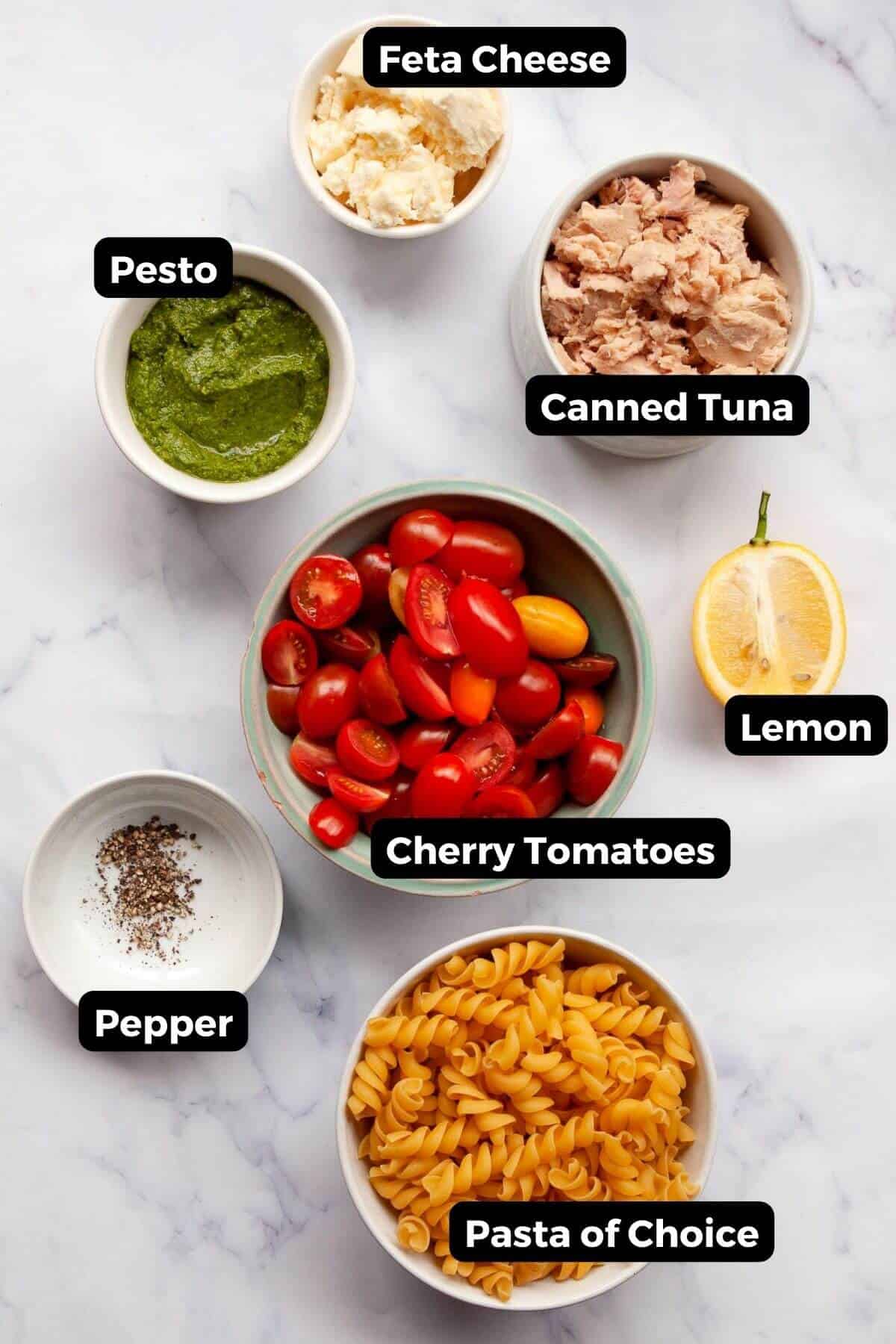Labeled ingredients for tuna pesto pasta including canned tuna, pesto, feta, cherry tomatoes, lemon, and pasta.
